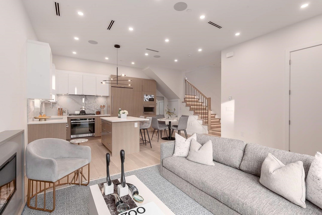 A modern living room featuring light colors, a comfortable sofa, and a well-lit, open kitchen area.