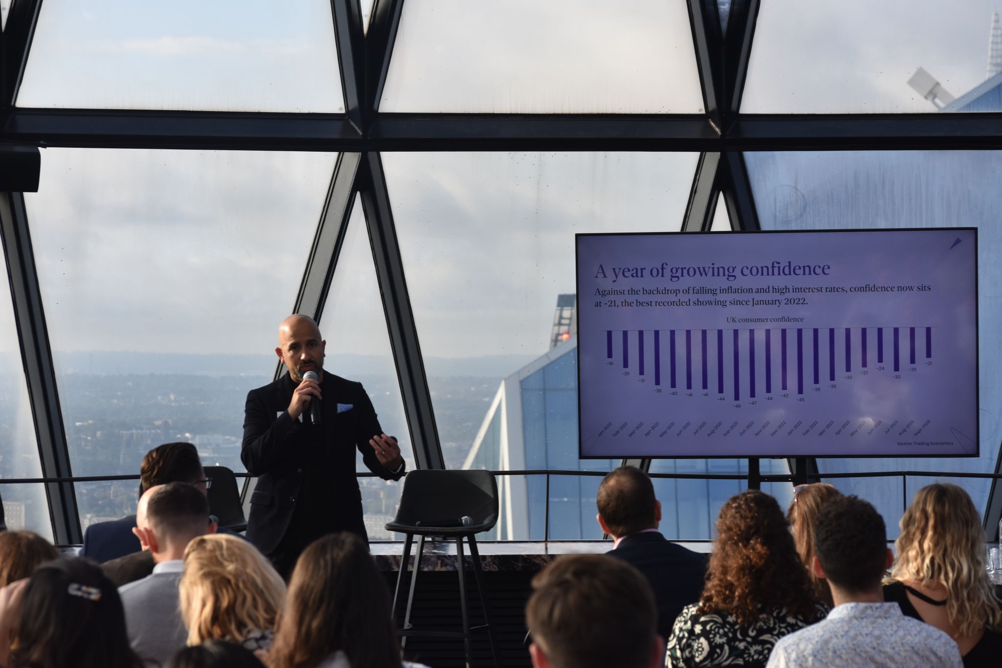People seated at a table with laptops and water bottles, engaged in discussion in a bright meeting room.