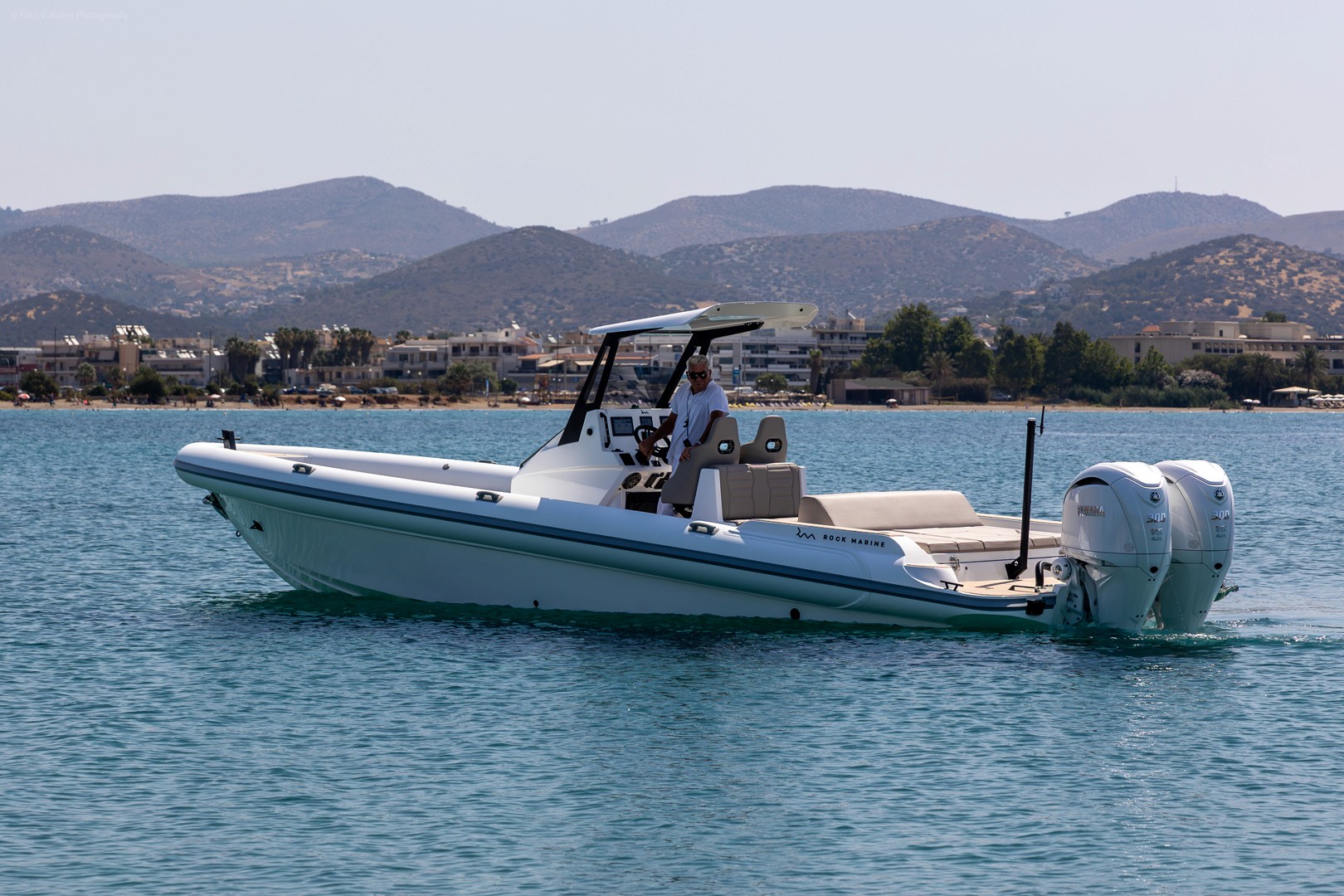 White Rock 36 speedboat with captain at helm cruising calm blue waters near Paros coastline with hills in background.