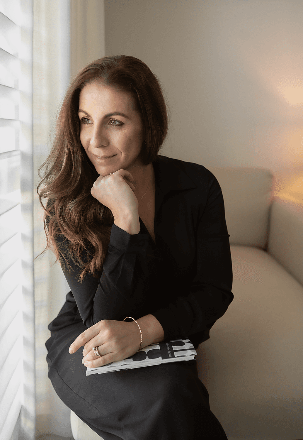 Casual studio portrait of a bearded man with curly hair in a white shirt, arms crossed, on a light gray background.