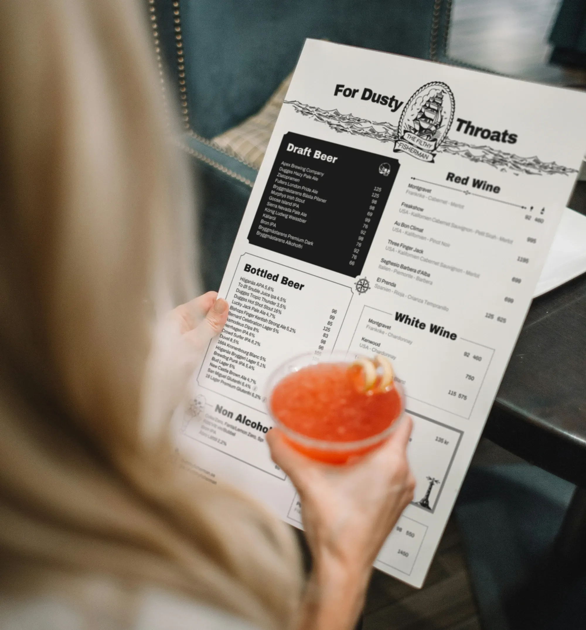 En kvinna som dricker en drink och tittar på The Filthy Fishermans dryckesmeny