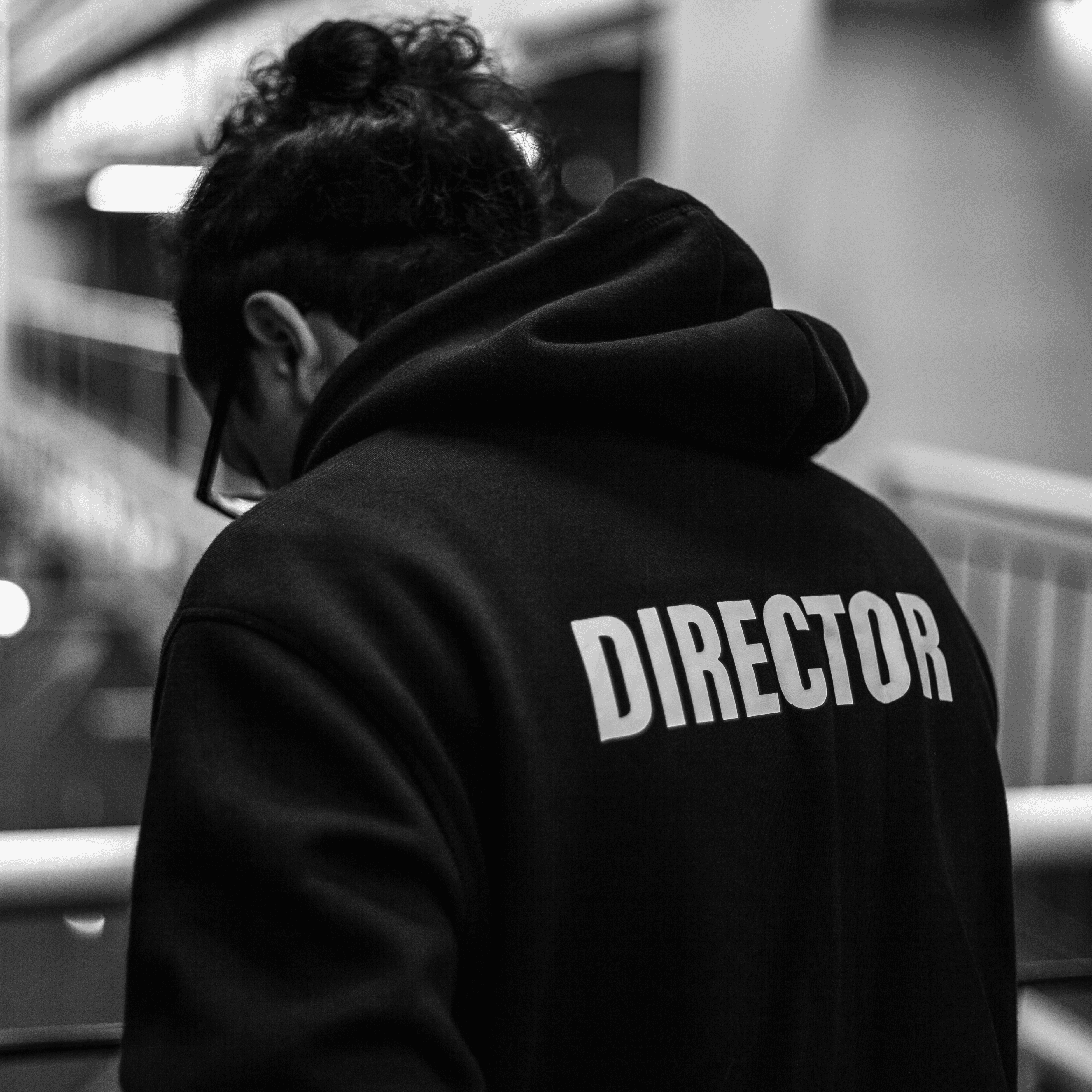 Director wearing a hoodie labeled ‘DIRECTOR’ while overseeing a production in a studio environment.