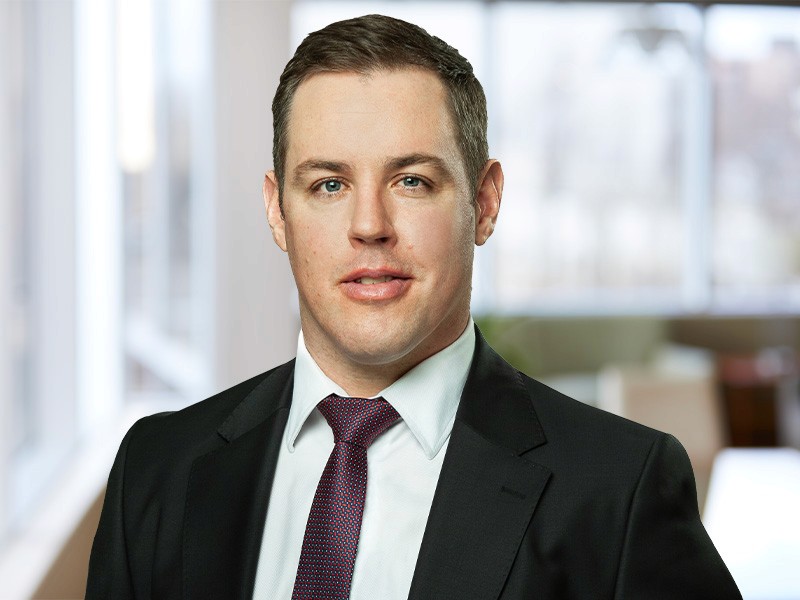 Headshot of a woman with shoulder-length brown hair, wearing a gray blazer and a light-colored top. She's smiling and has a professional look.