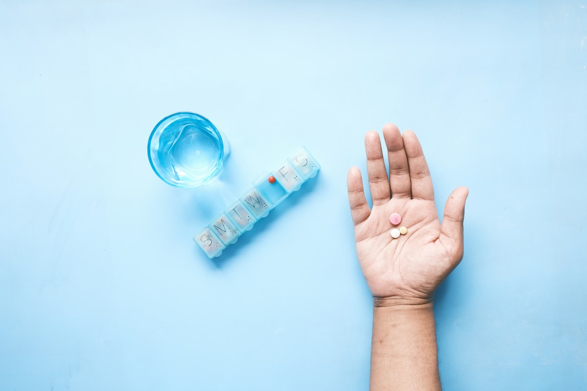 A single supplement tablet in an open palm beside a glass of water, illustrating a low-and-slow start.