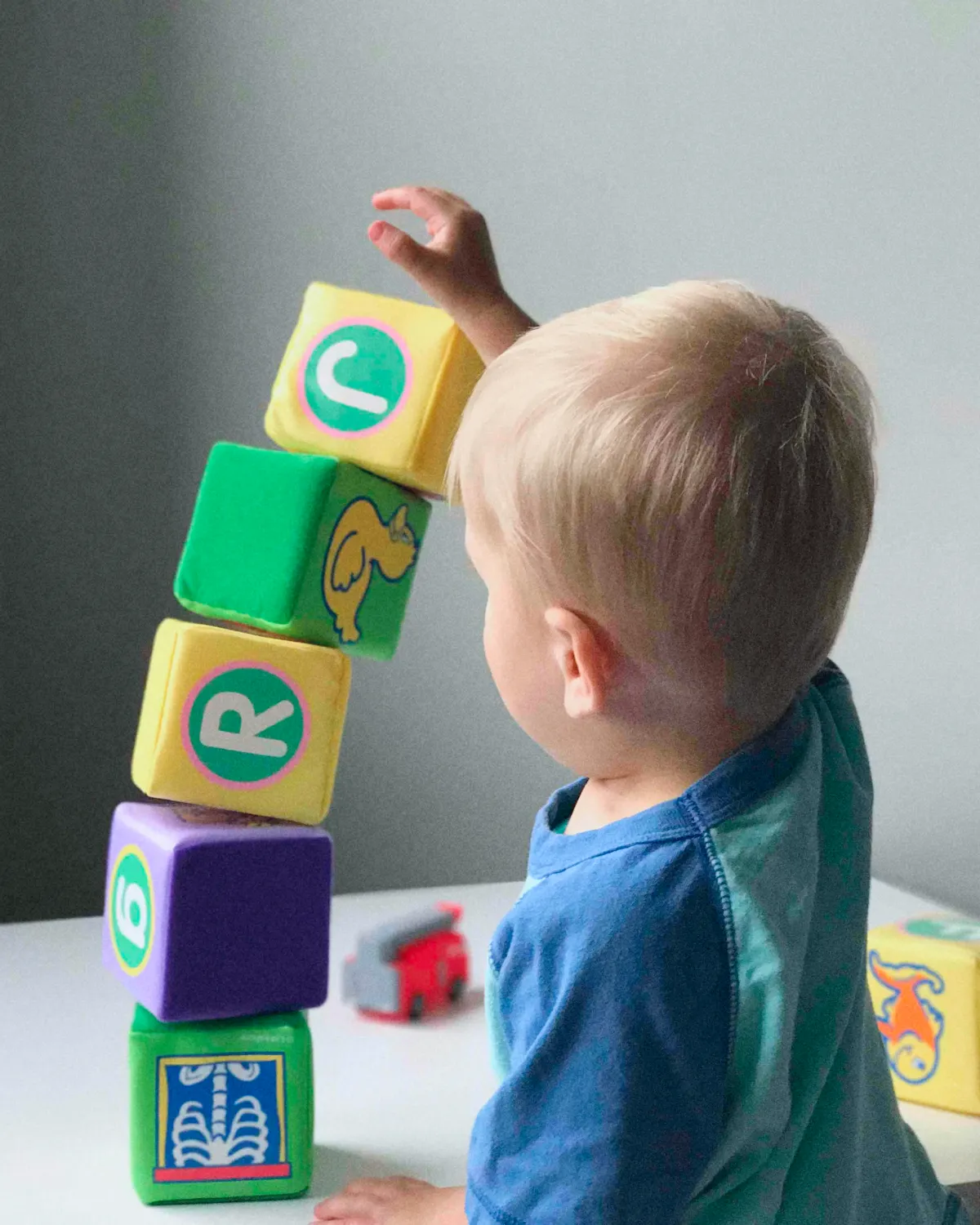 boy toddler playing with colorful lettered cubes on a table.