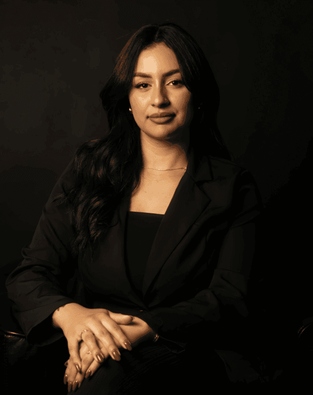 Young person with short, tousled blonde hair wearing an oversized, vibrant orange turtleneck sweater against a soft grey background, conveying a cool, modern look.