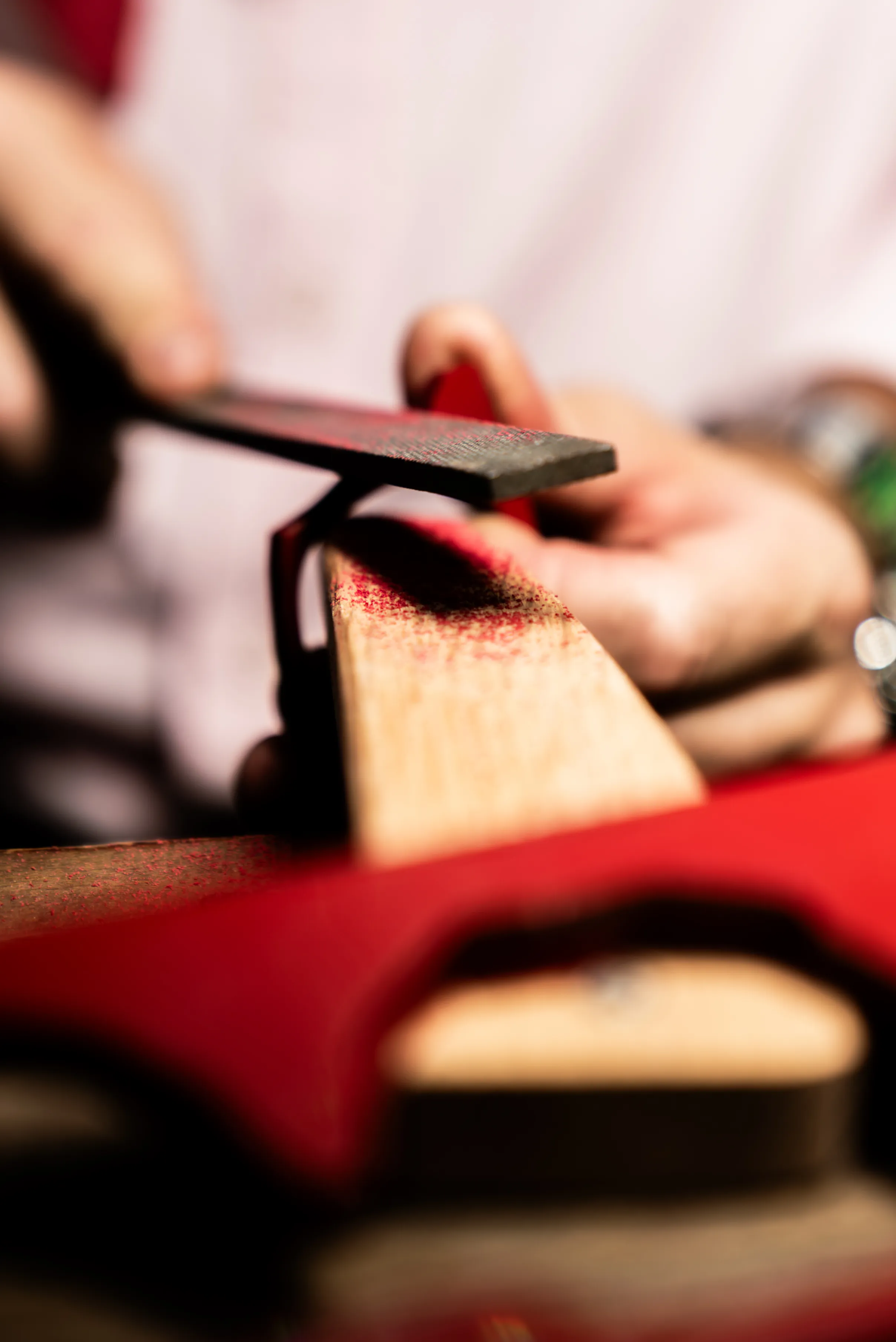 Artigiano durante la lavorazione manuale di una montatura IDIA rossa con lima professionale, in una fase di sagomatura e rifinitura dell’occhiale. L’immagine mostra il processo artigianale con cui il progetto su misura di Ottica Dentella ad Ancona passa dal disegno alla materia, attraverso lavorazioni precise che definiscono forma, superfici, proporzioni e dettagli della montatura.