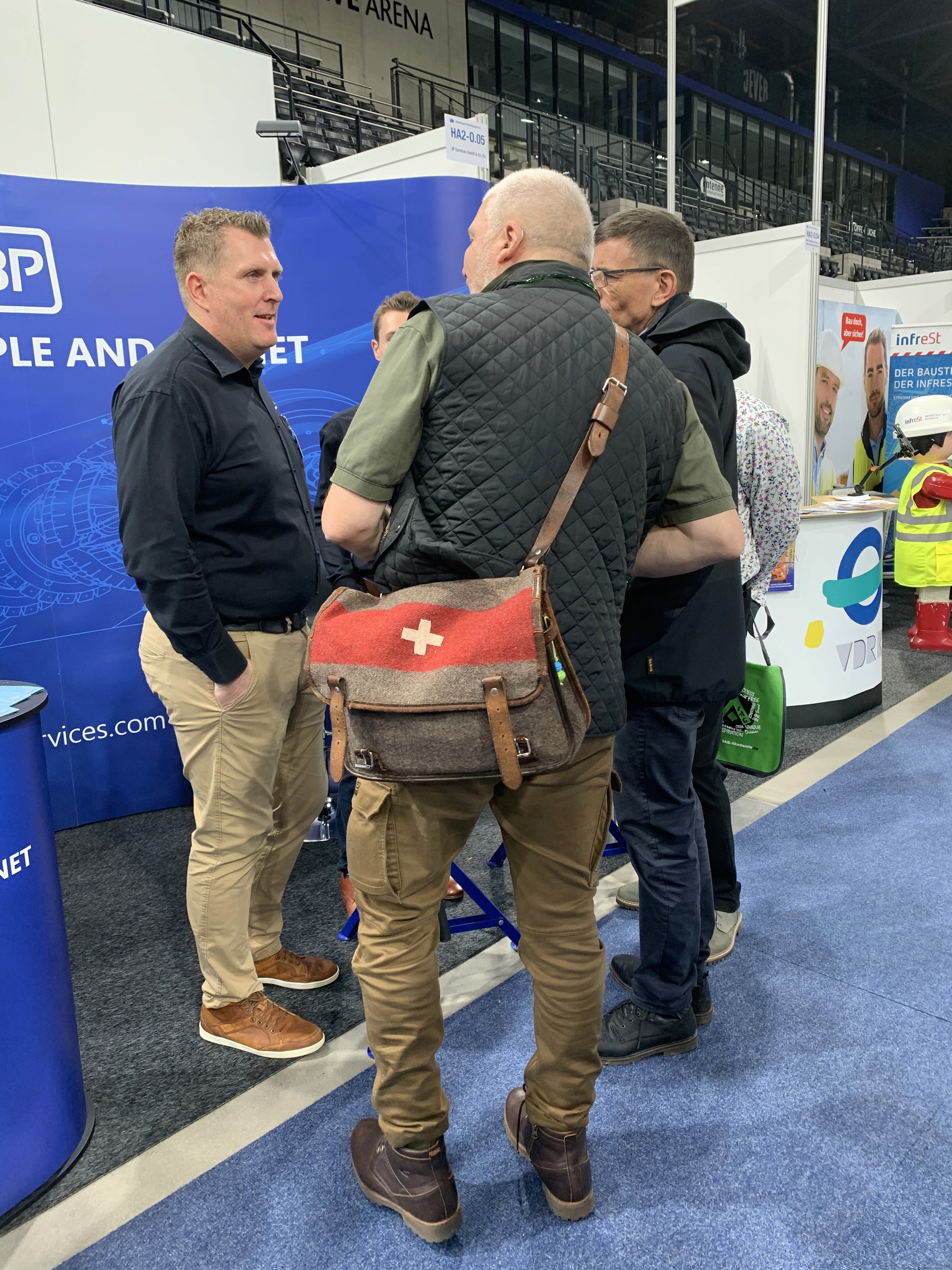 Attendees sit at a booth promoting 30+ years of IJJ experience. Booth includes signage, product images, and brochures.