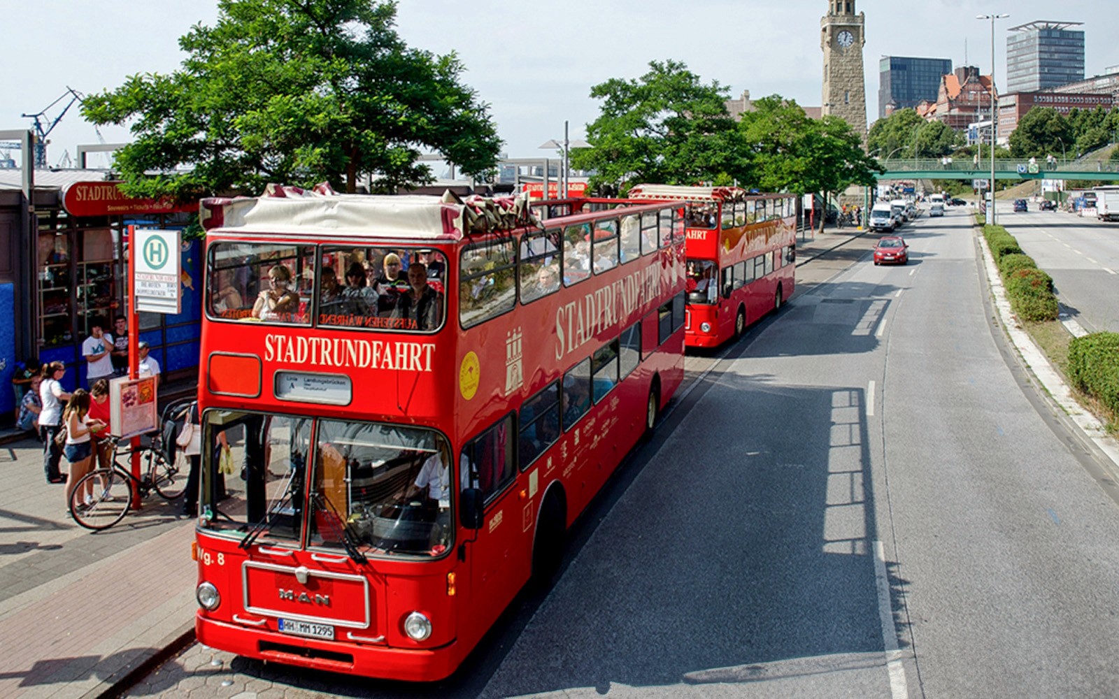 Rote Doppeldeckerbusse für Stadtrundfahrten in Hamburg, Deutschland, in der Nähe eines Uhrturms, Teil des Hamburg City Passes.