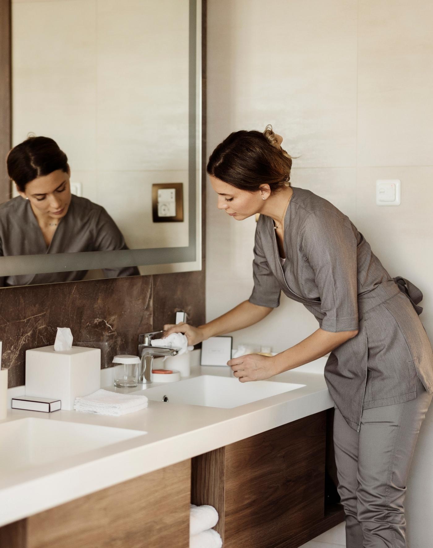 A person in a stylish bathroom is washing their hands at a sleek countertop while looking in the mirror.