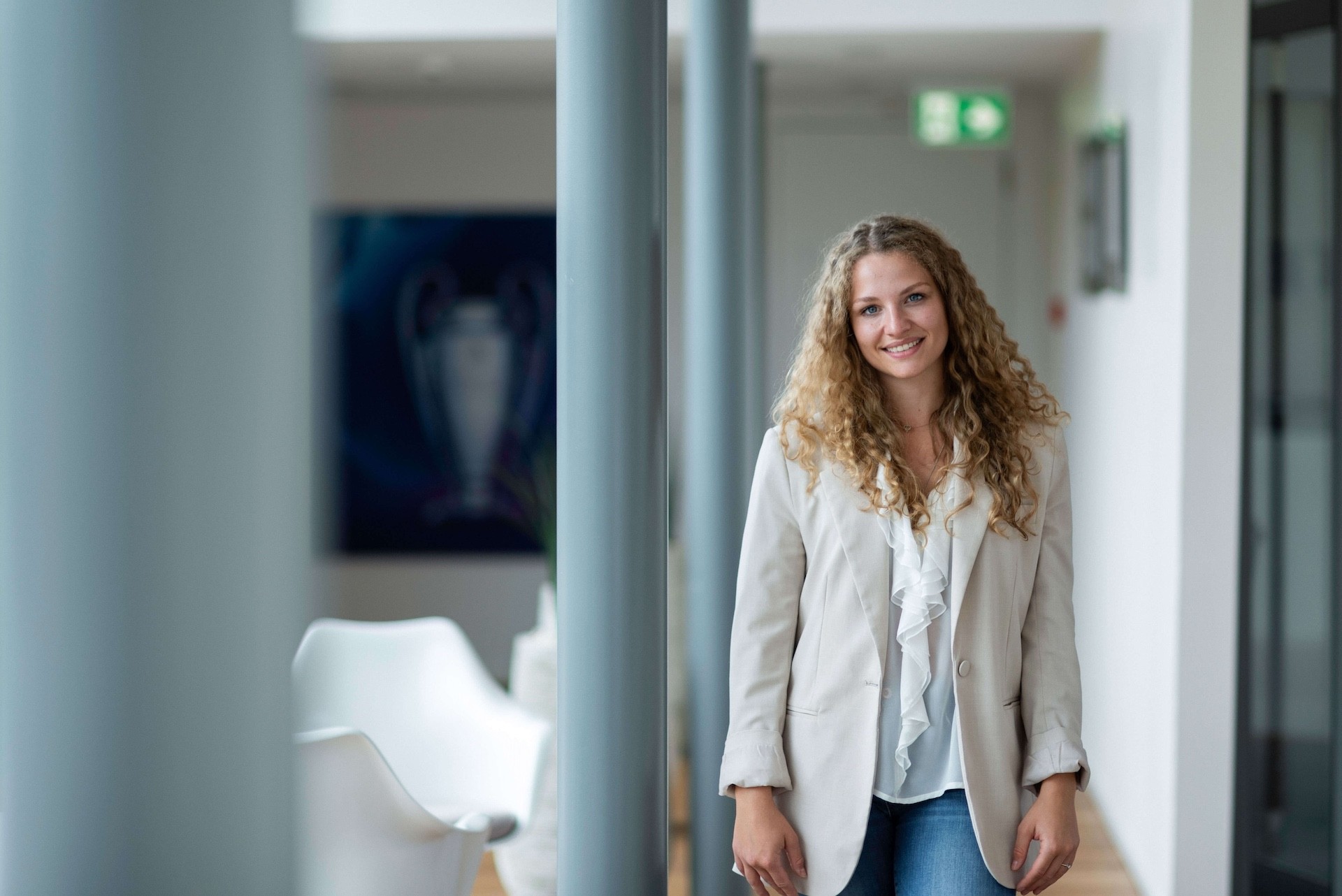 Smiling woman from Team standing confidently in a hallway, conveying a warm and professional presence.