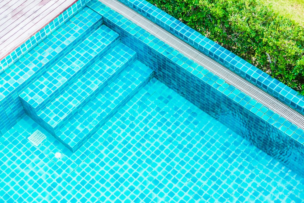 Bright turquoise swimming pool with mosaic-tiled steps leading into the water.