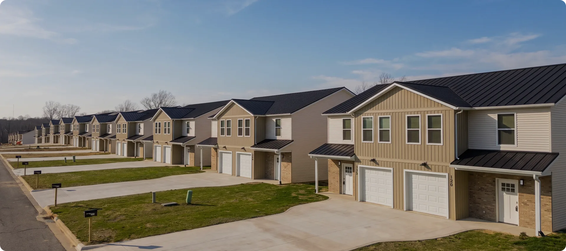 Brushwood Duplex: a long row of tan and grey two-story duplex homes with dark metal roofs, awnings and paired garages along a shared driveway