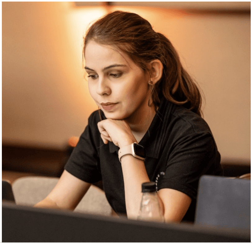 Editorial portrait of a young man with wavy hair in a knit sweater, looking over his shoulder in soft light.
