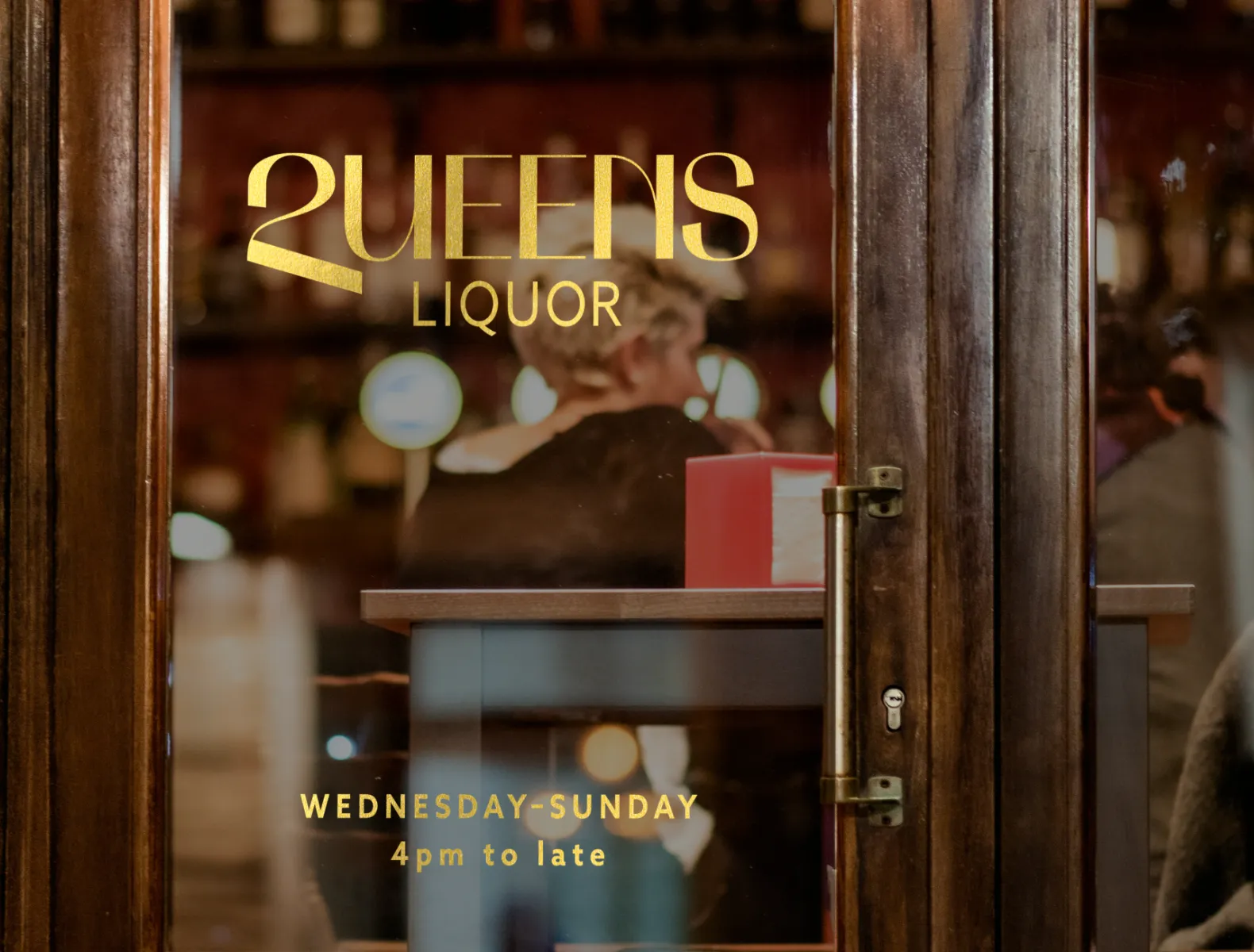 The Queens Liquor wordmark in gold foil on a bar door. 
