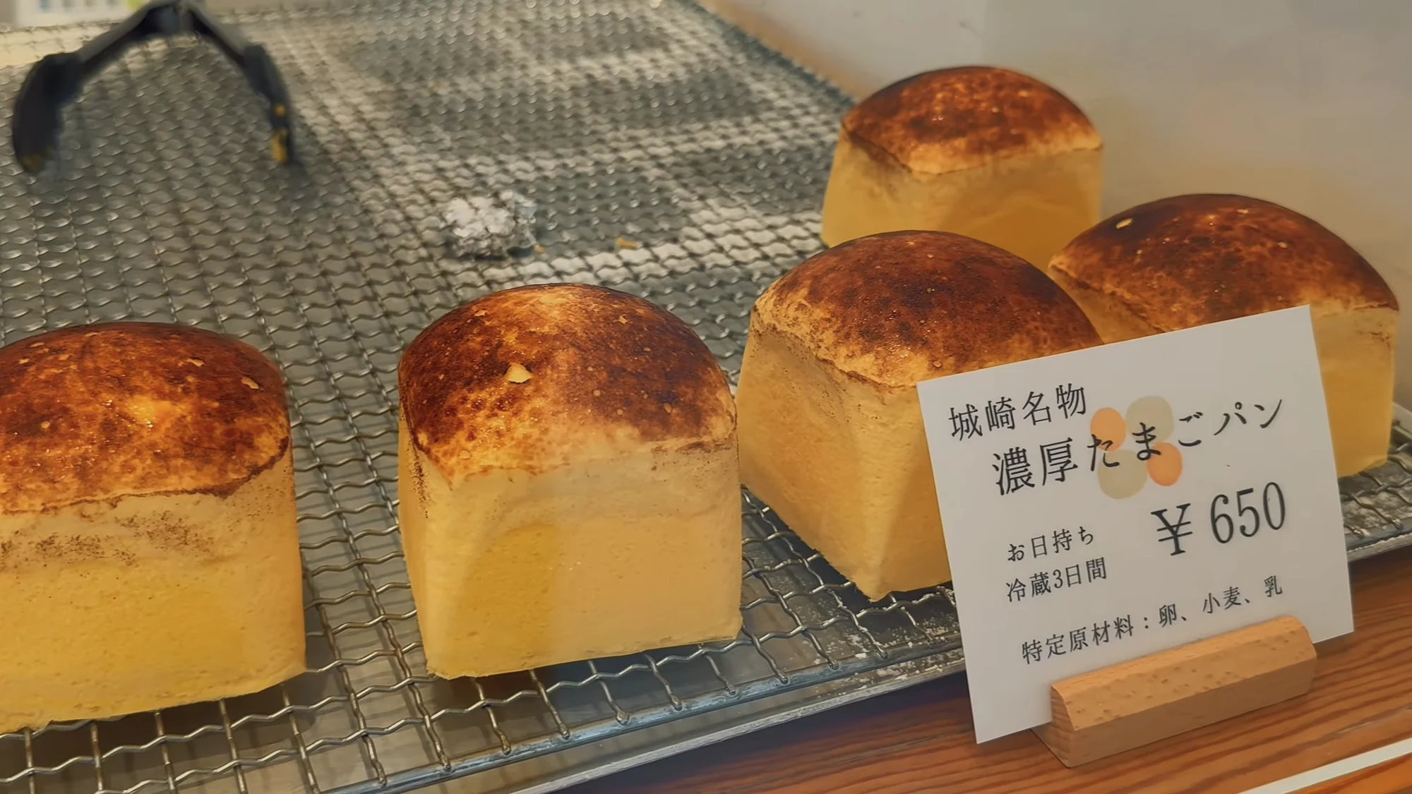 Four small loaves of Kinosaki's rich egg bread on a wire rack with a price card.