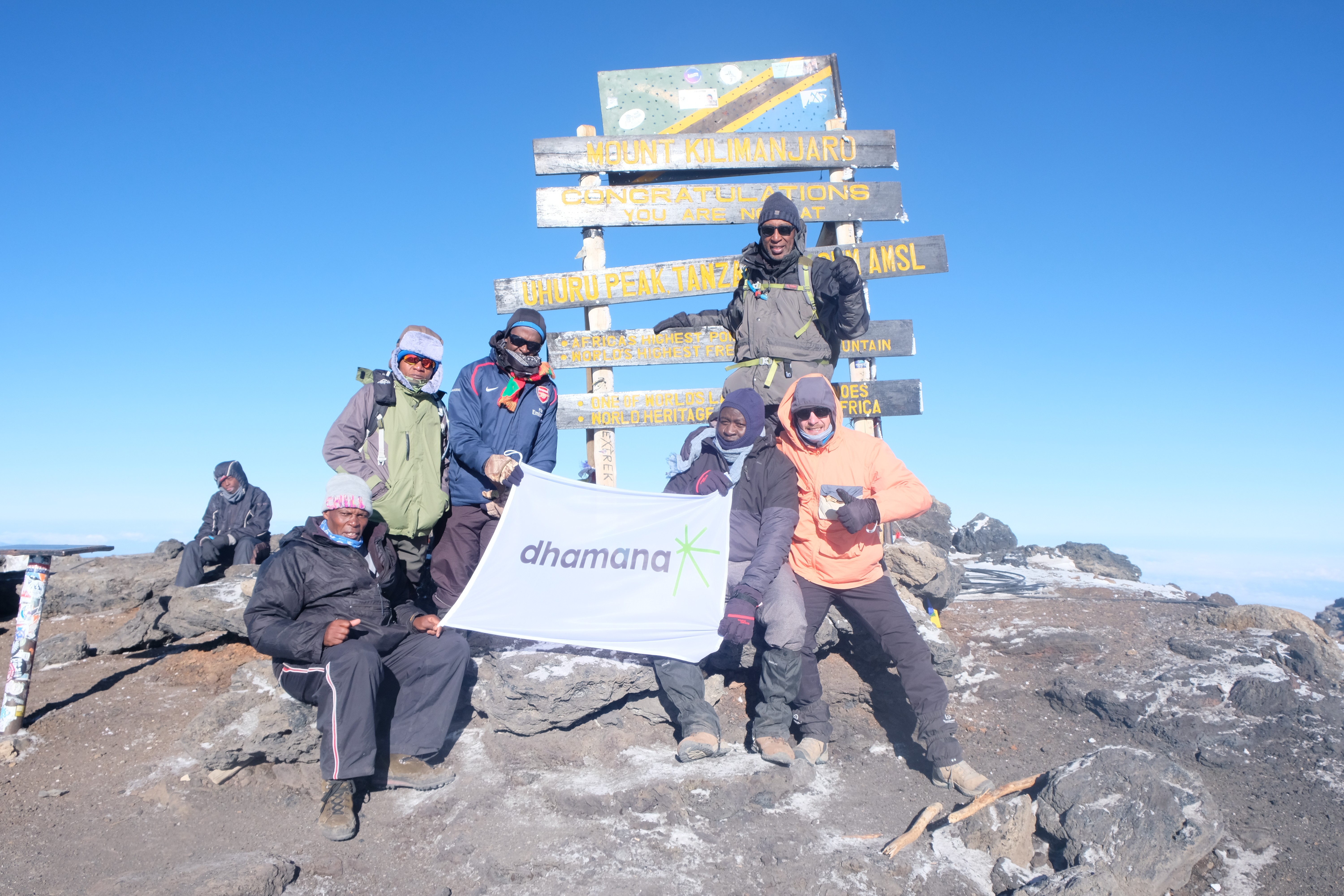 Dhamana Flag being held up by people by a mountain kilimanjaro summit billboard