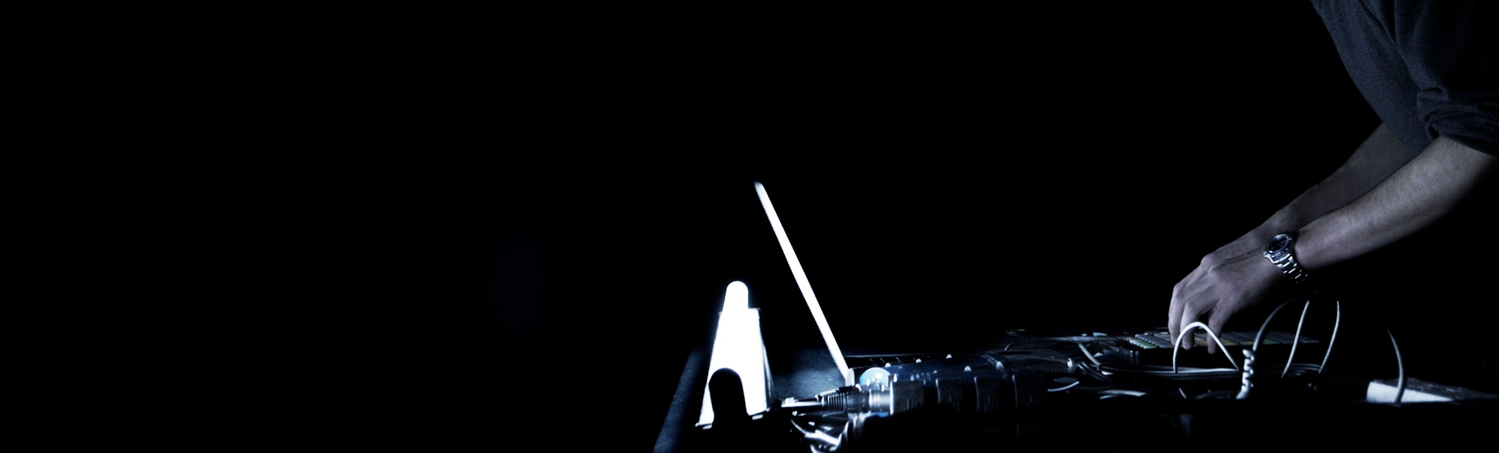 Hands on music equipment, lit by a laptop in the dark.