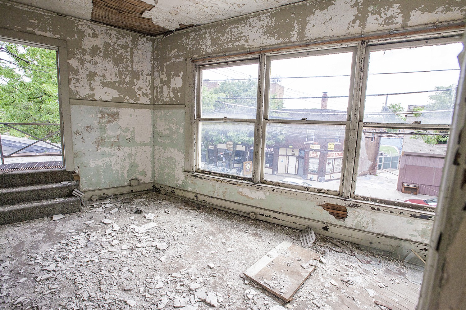 An empty room with bare walls, large windows, and a concrete floor, featuring natural light and greenery outside.
