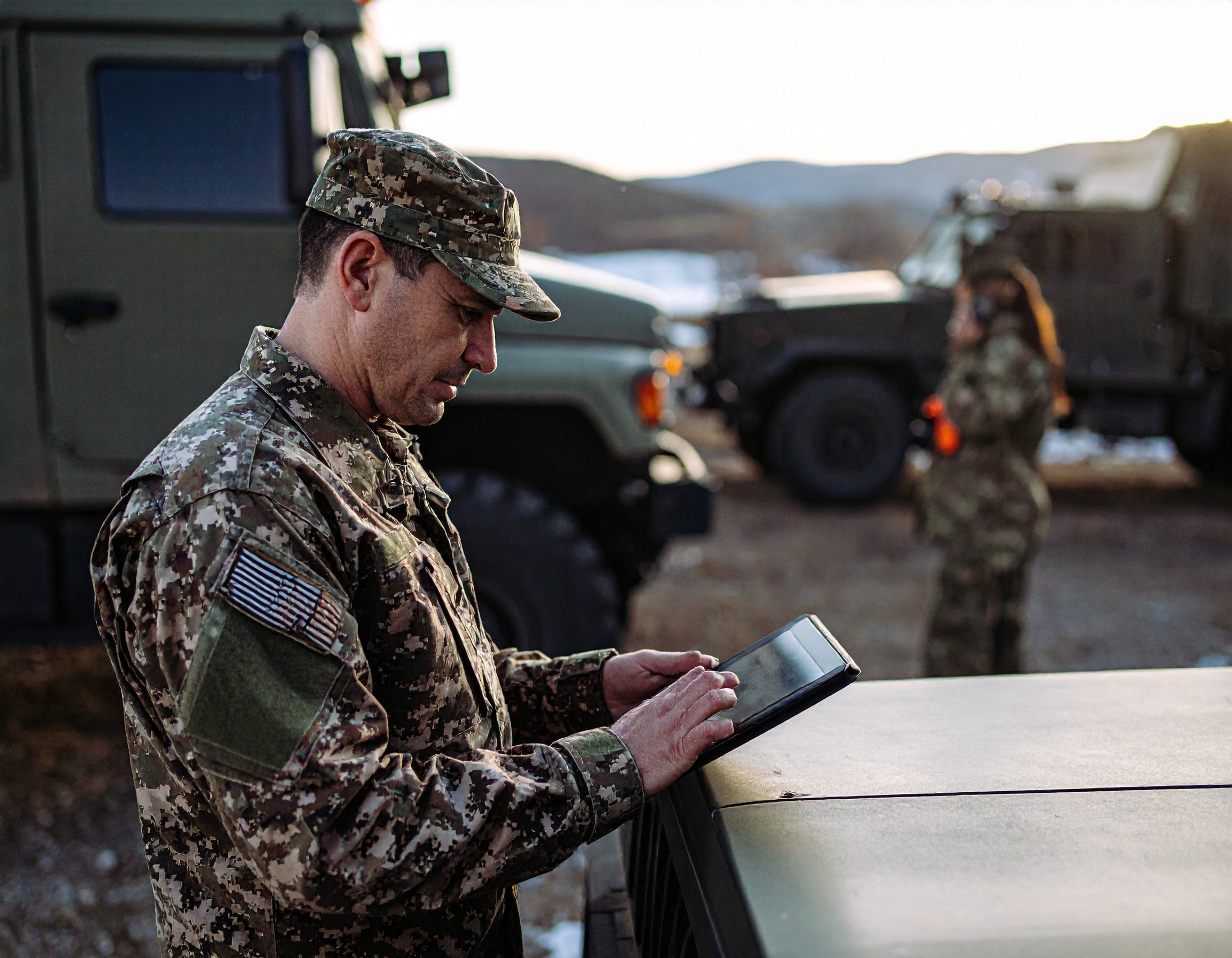 sodlier checks tablet, vehicles in back