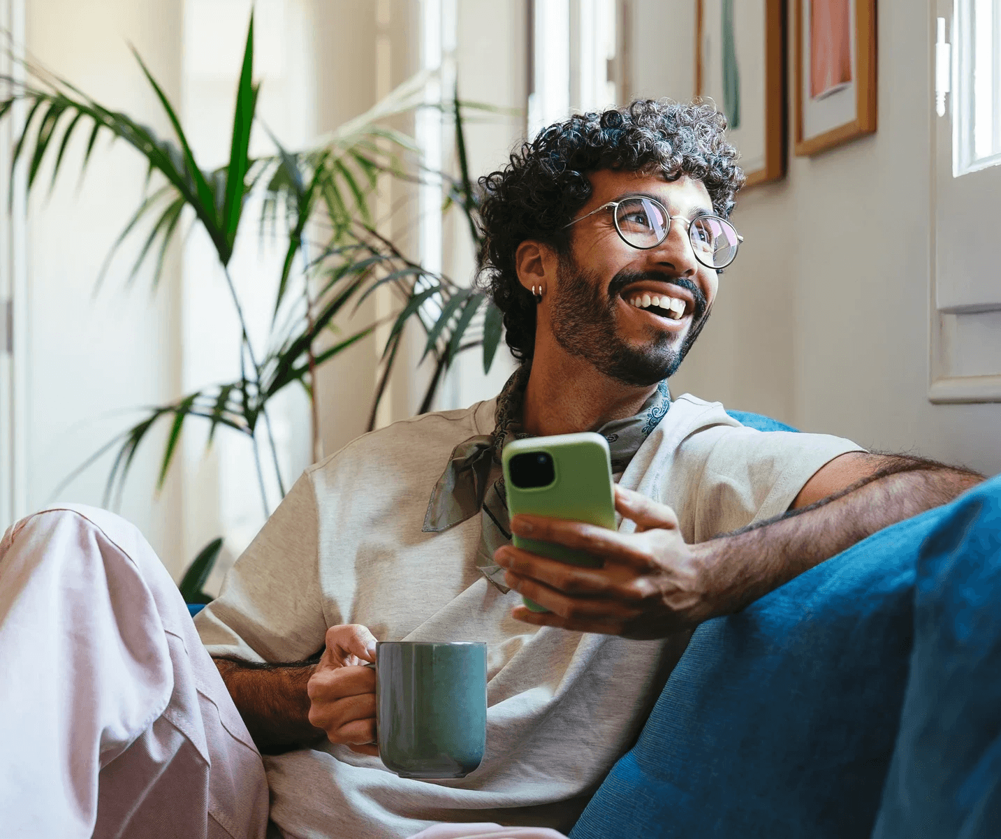 A retirement saver sits on a sofa with a mug and cell phone, looking aside while considering the Pontera platform.