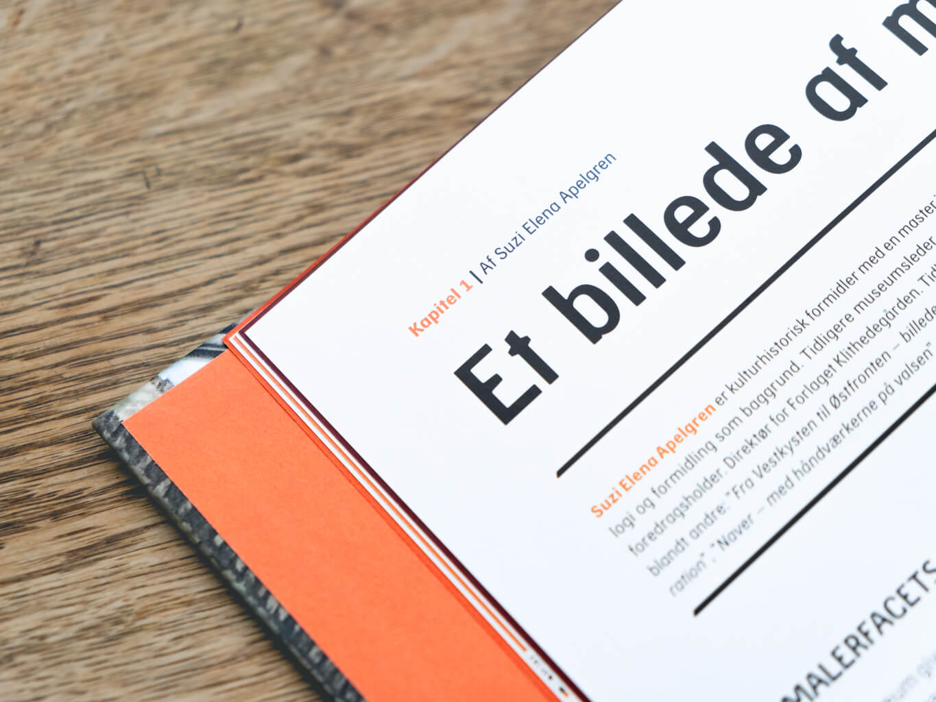 Close-up af en åben bog. Der står "Kapitel 1: Ad Suzi Elena Apelgren. Et billede af..."