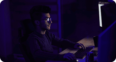 Cybersecurity specialist working late at a computer monitor in a dark office focusing on risk compliance and audit trails.