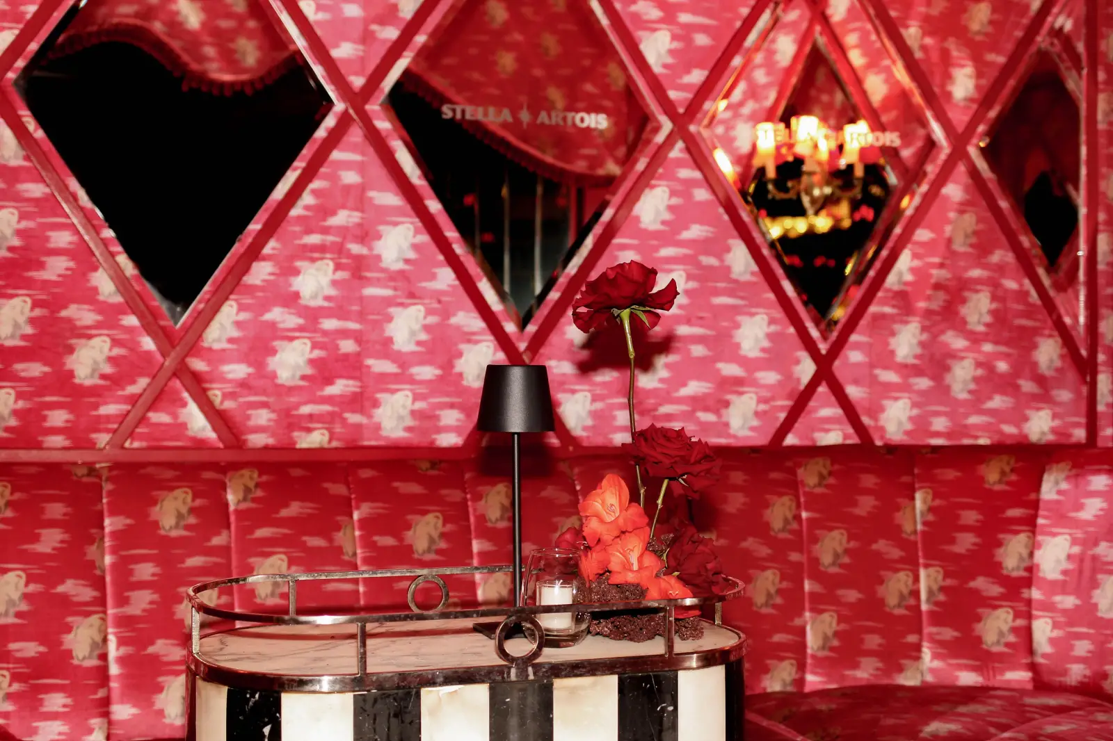 Decoración de interiores con sillones rosas, espejos romboidales y flores rojas.