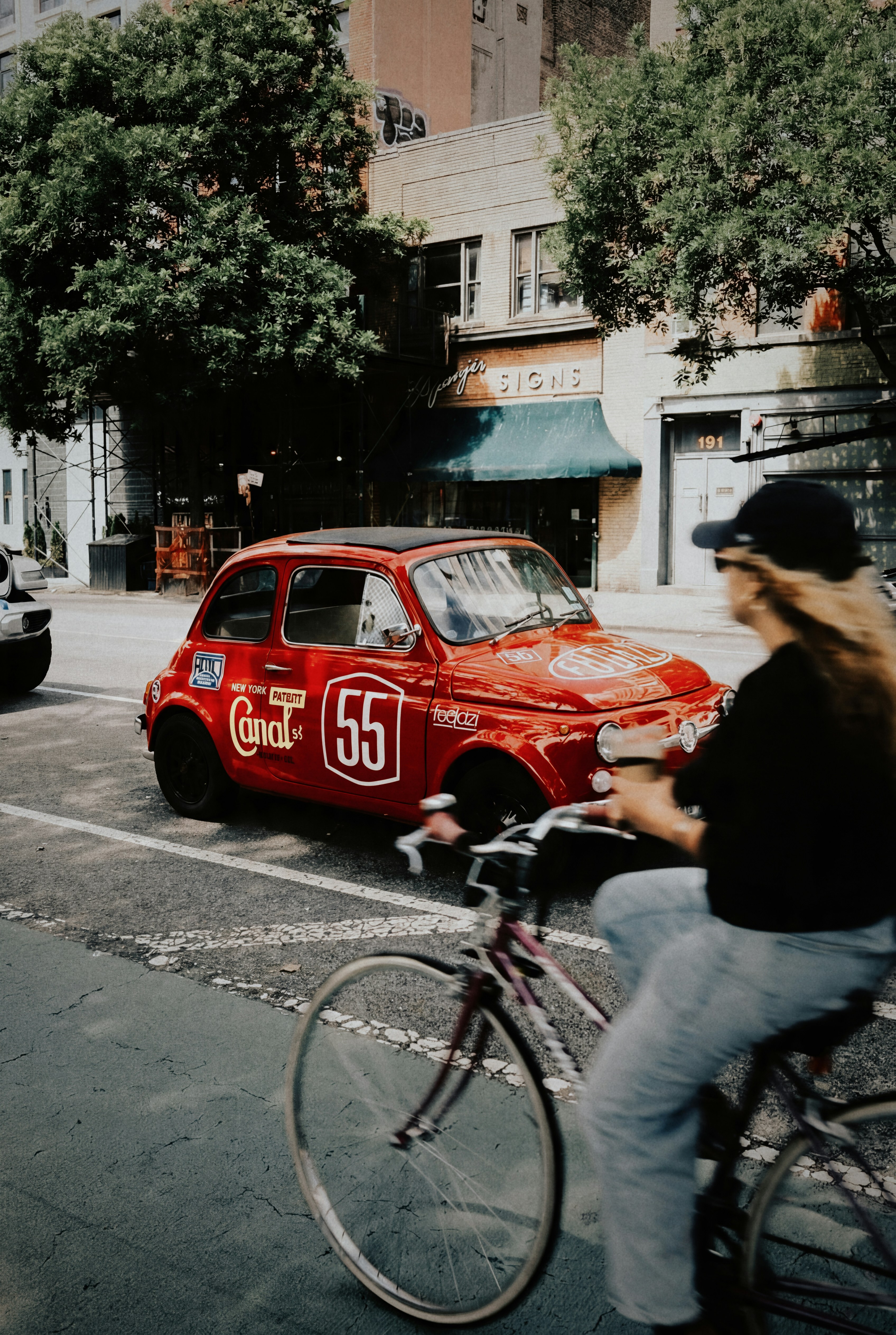 A red vintage car and cyclist on a city street.