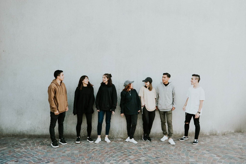 Diverse group of young adults in casual outfits standing against a minimalist wall.