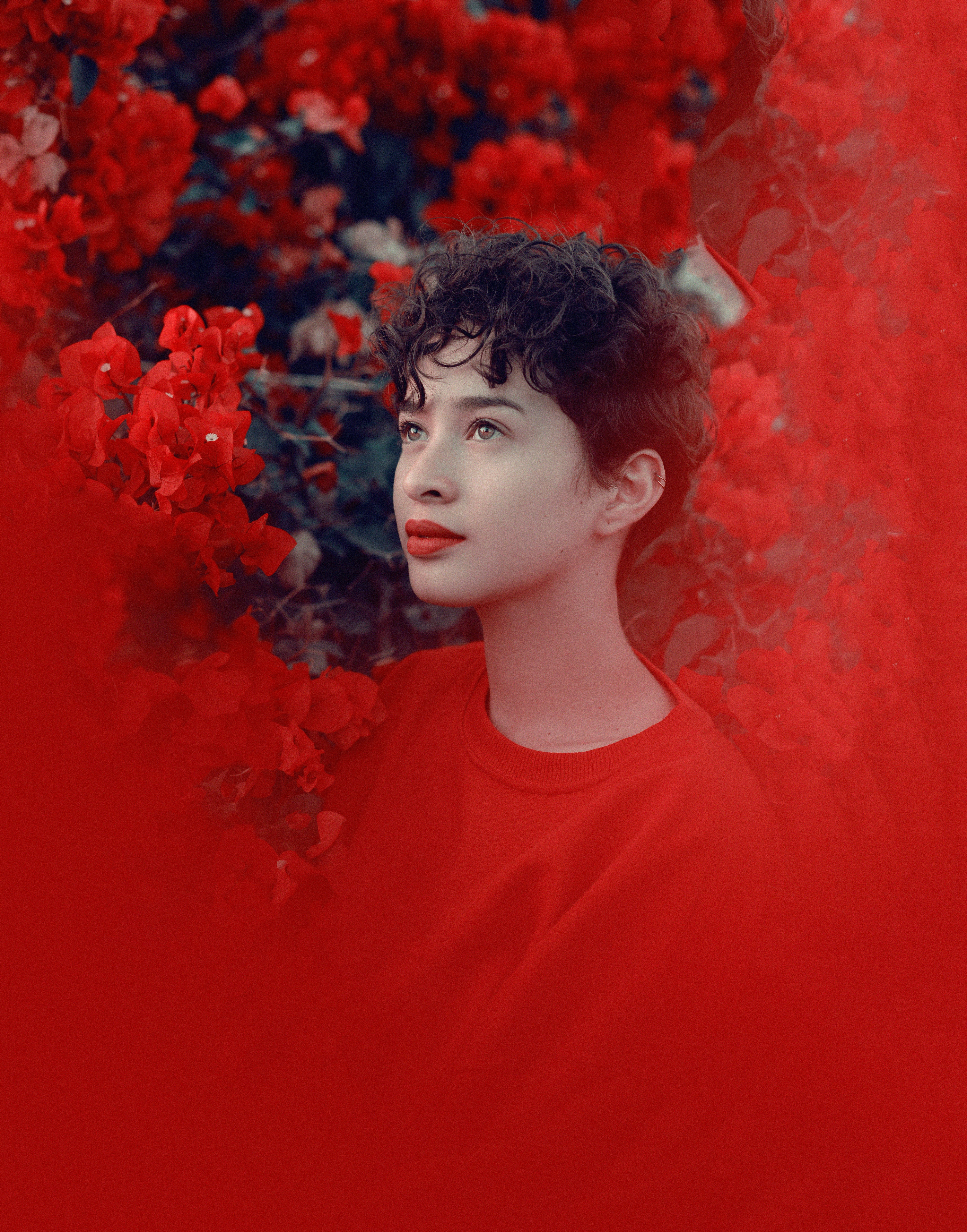 girl in red crew neck shirt standing beside red flowers