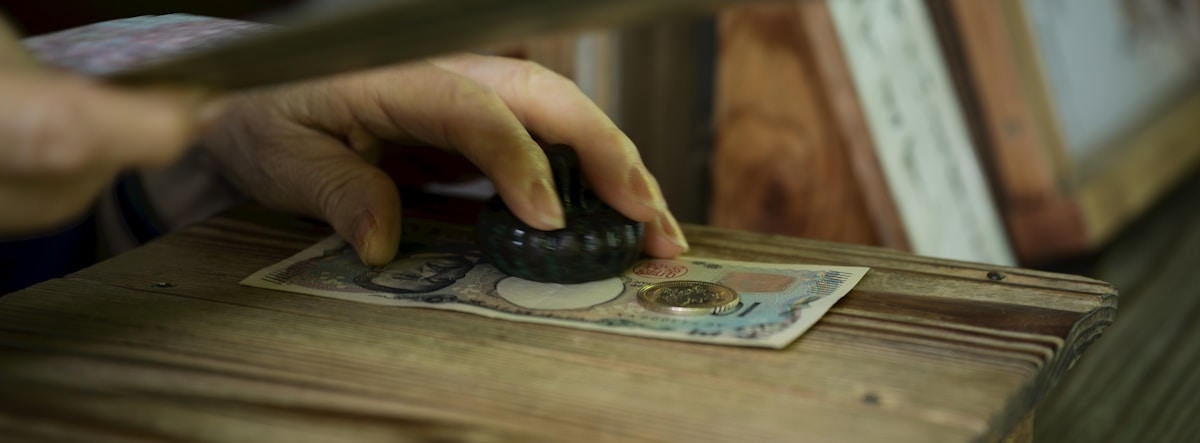 Hand placing a Japanese banknote and coin on a wooden counter