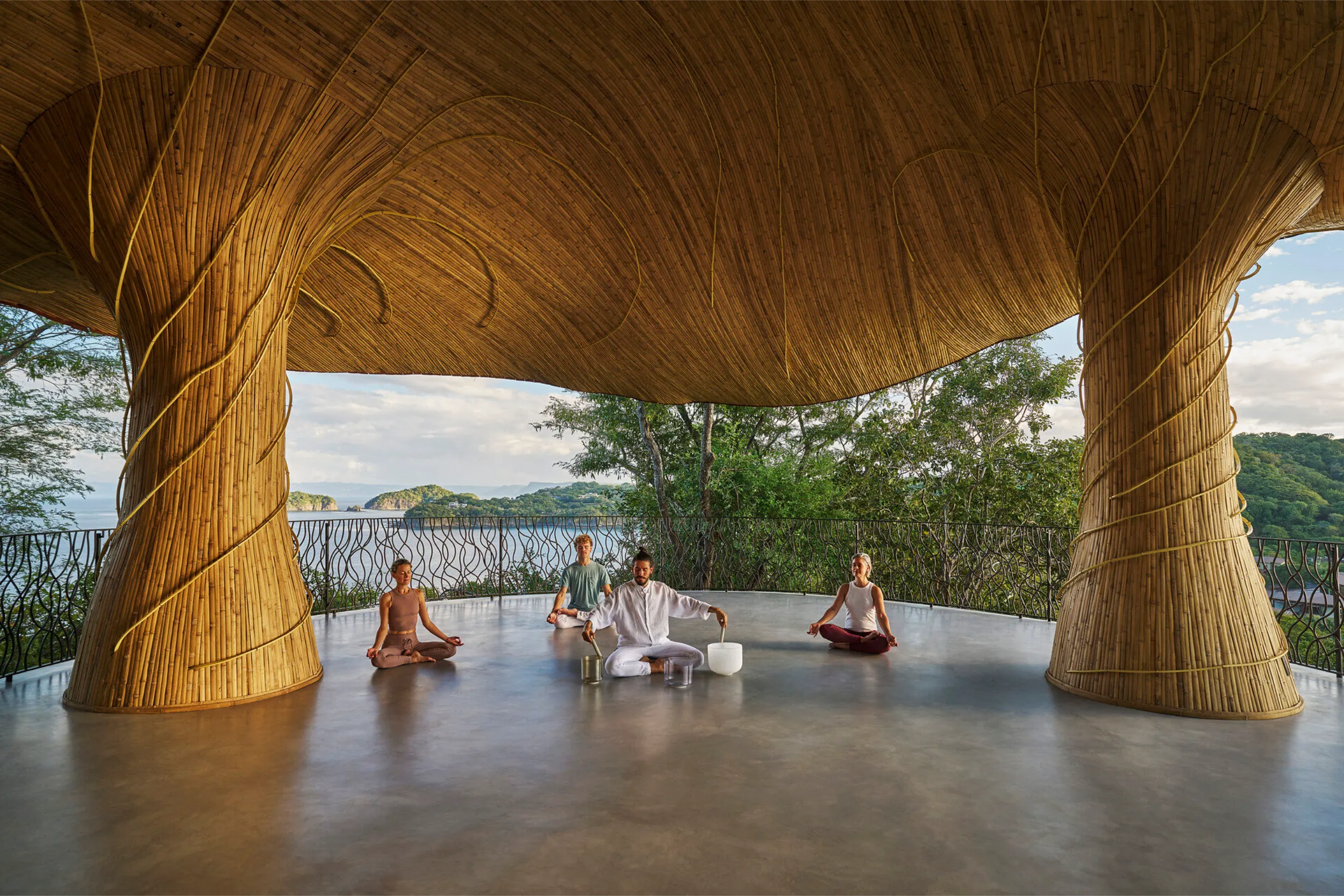 Group sound healing session inside the Four Seasons bamboo pavilion, showcasing the massive branching bamboo columns and panoramic ocean views.