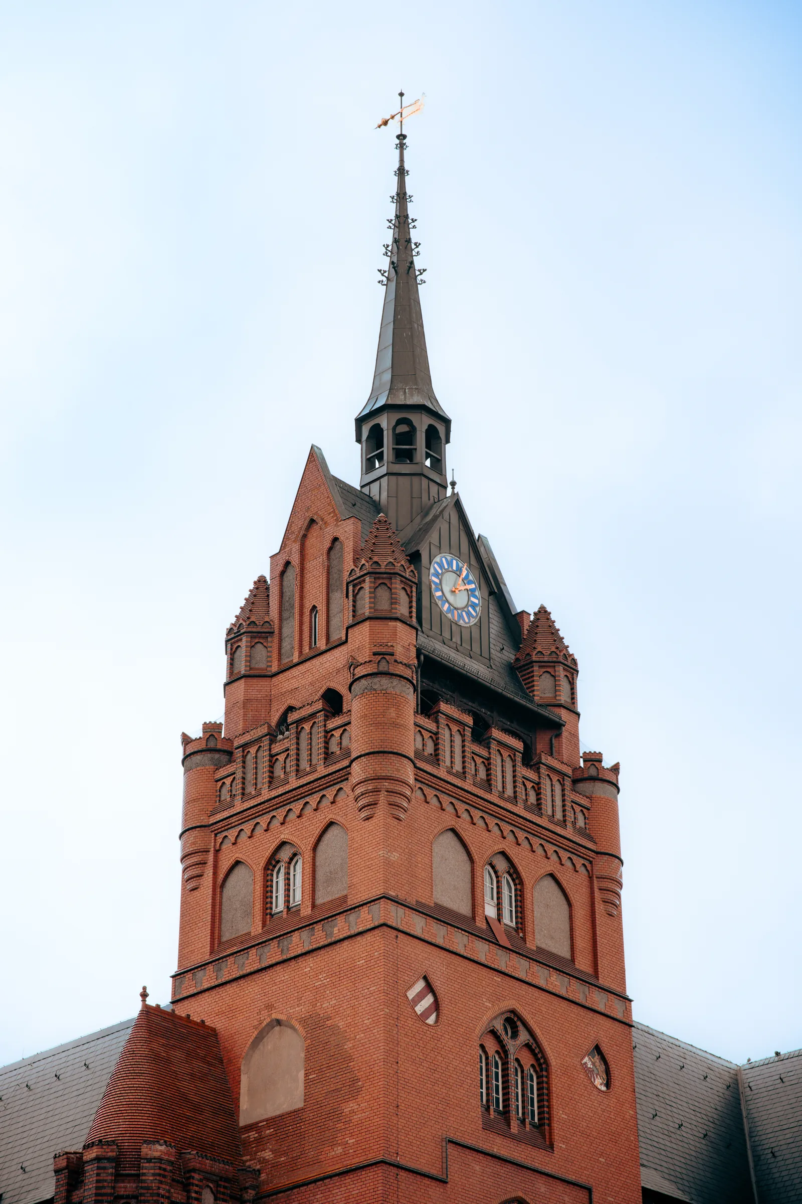 Der markante rote Backsteinturm des historischen Rathauses Steglitz im neugotischen Stil mit einer blauen Turmuhr.