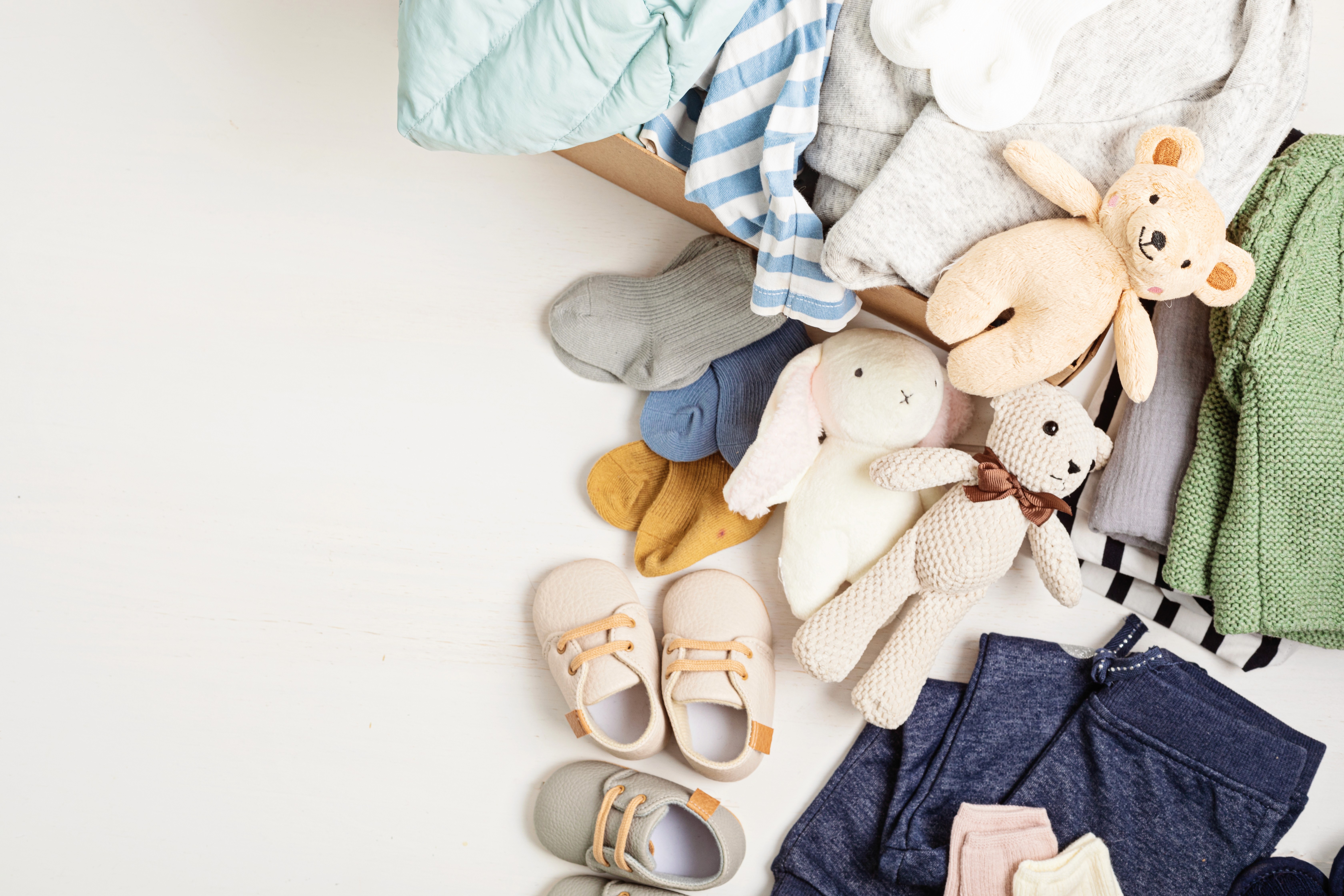 Baby Erstausstattung mit Kleidung, Spielzeug und Babyschuhen in einer Kiste – Übersicht für eine praktische Baby Erstausstattung Liste.