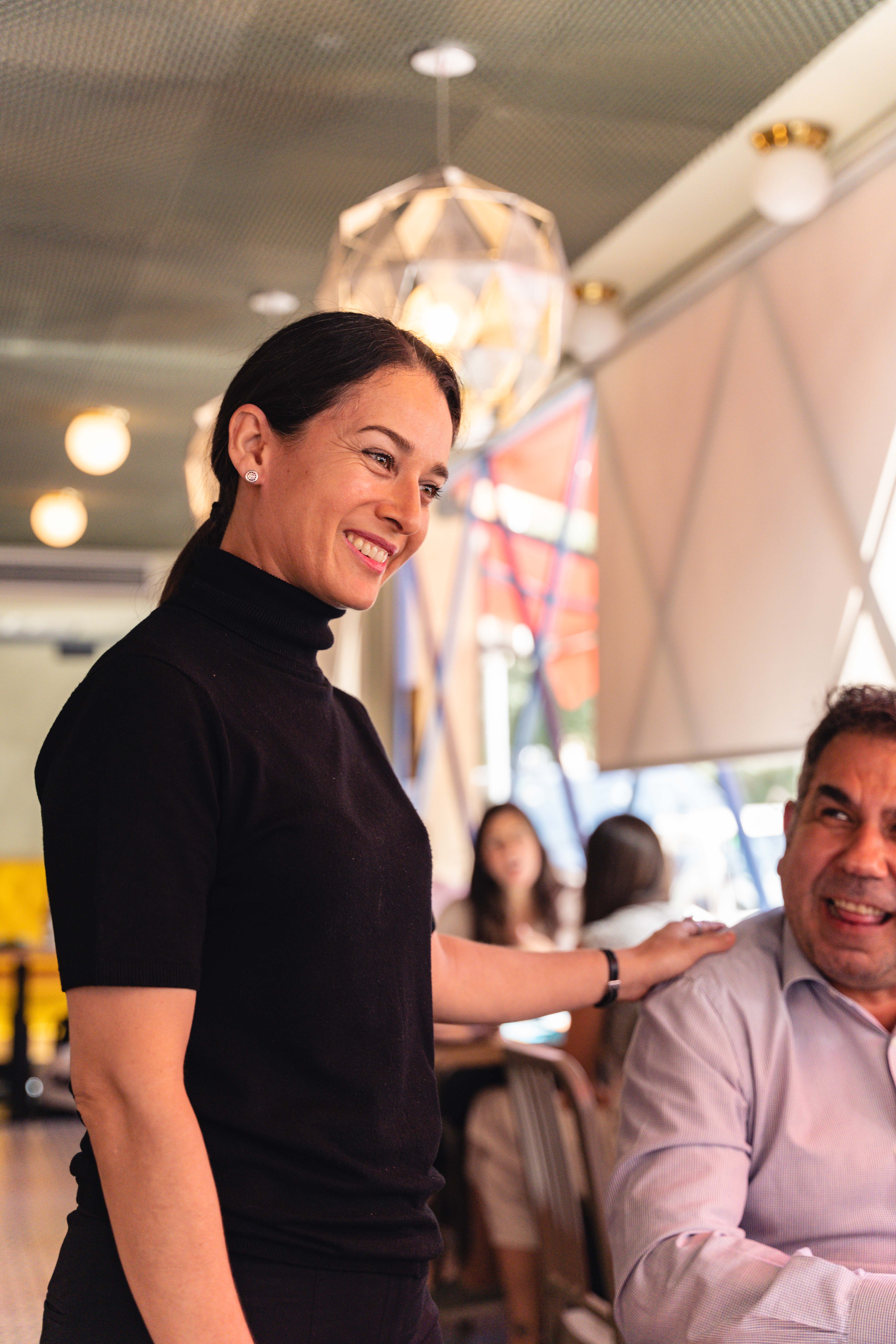 Mujer sonriente hablando de pie hablando con clientes sentados en una mesa