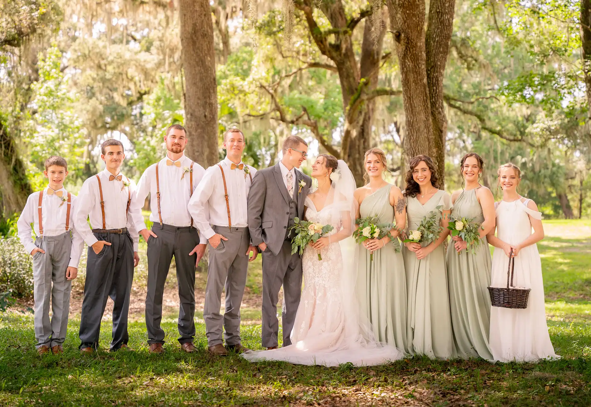  a wedding party standing under some beautiful trees with the bride and groom, looking at each other