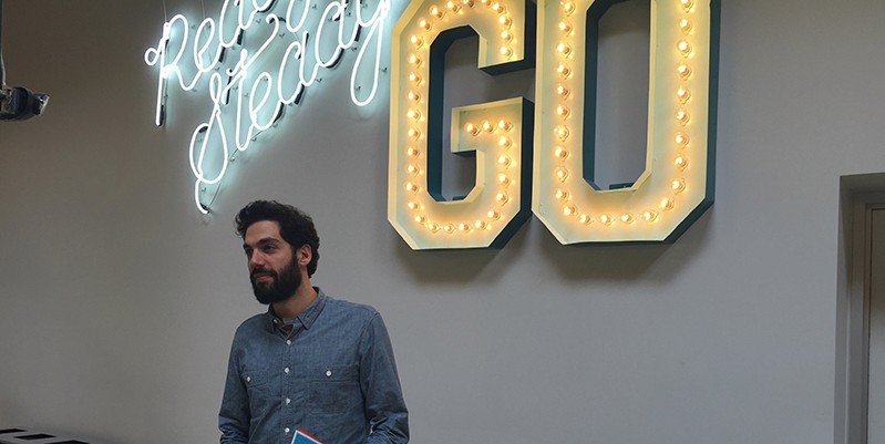 A photo of a man standing in front of an illuminated advertisement logo that says: Ready Steady GO..