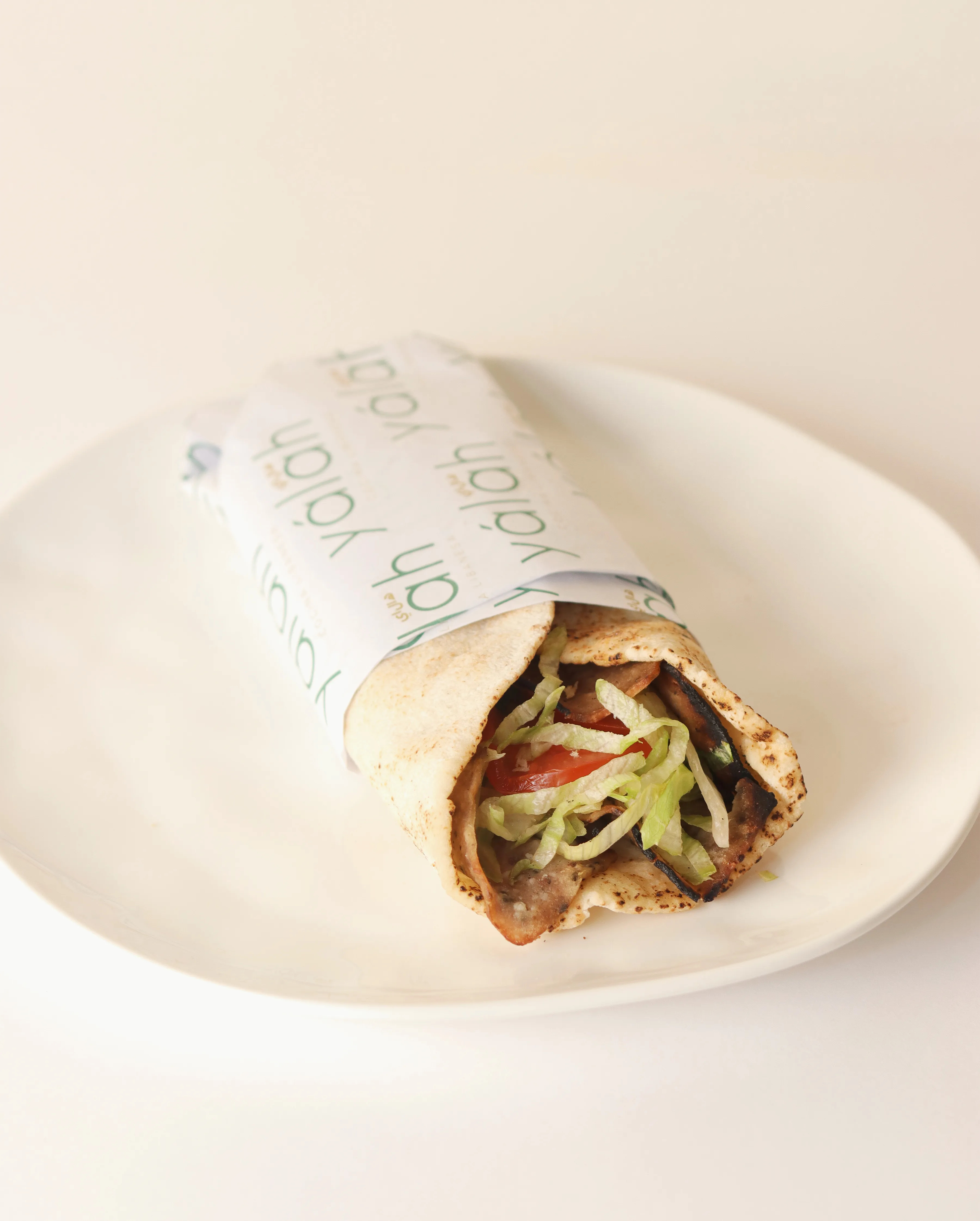 Shawarma envuelto en pan pita sobre plato blanco.