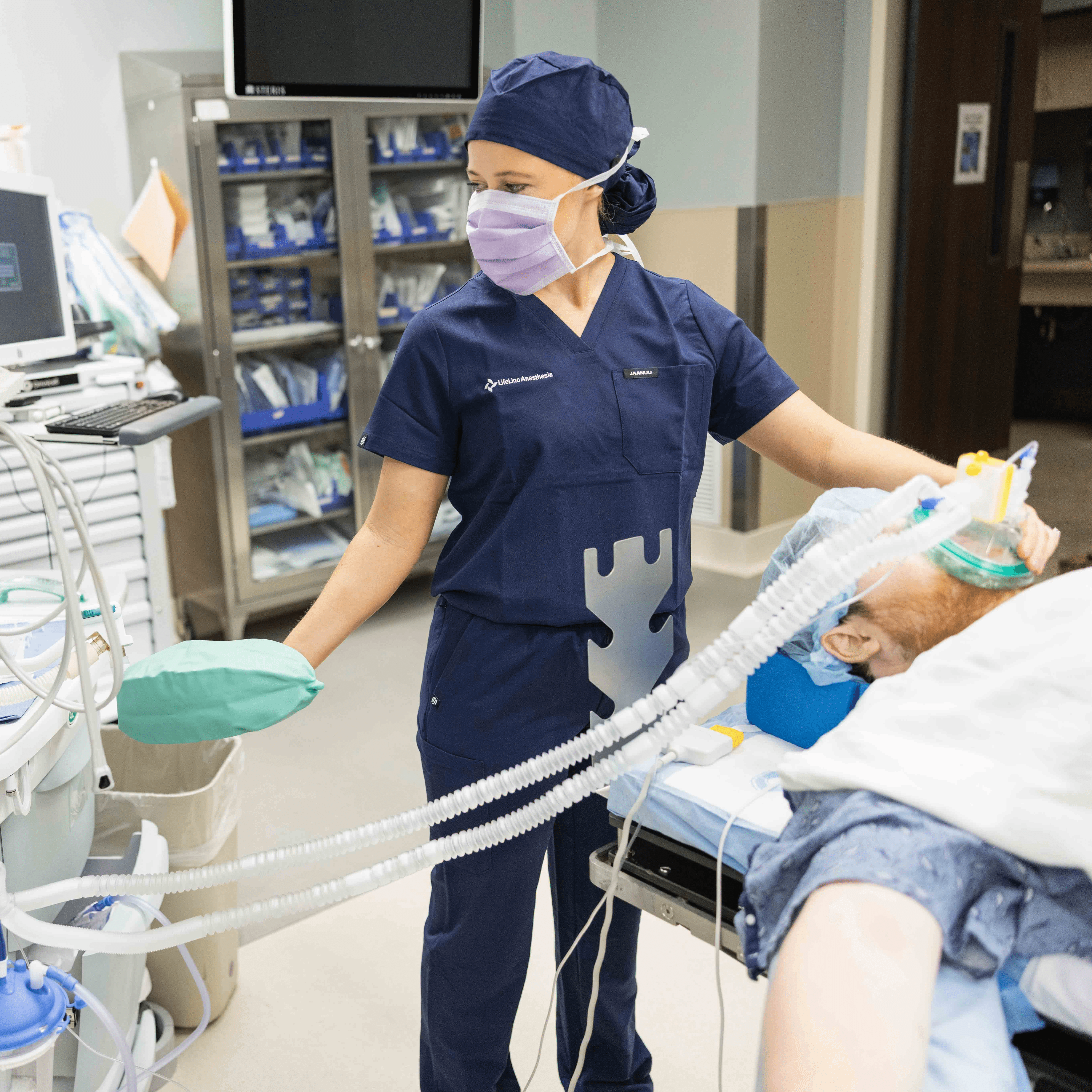 A LifeLinc CRNA in navy scrubs and a mask administers anesthesia to a patient in a clinical setting, representing PRN anesthesia staffing opportunities