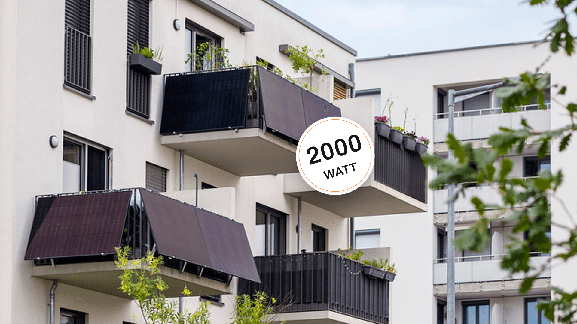 Modernes Wohngebäude mit mehreren Balkonen mit Photovoltaikmodulen und Grünflächen im Vordergrund.