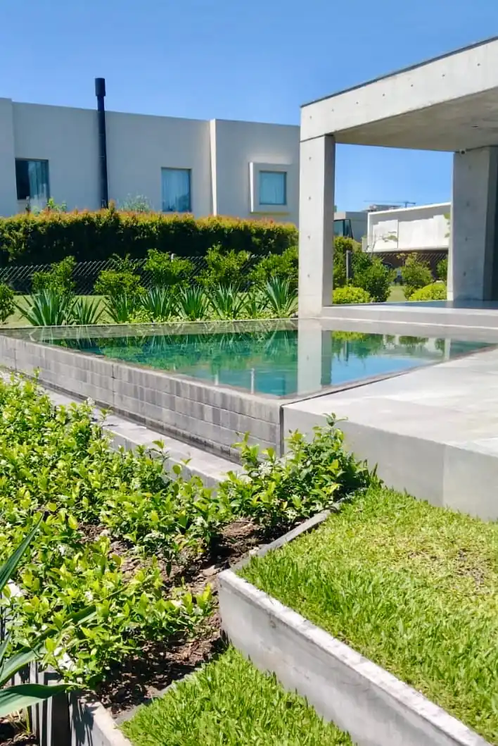 Moderna piscina elevada con diseño de borde infinito y agua color esmeralda, integrada perfectamente a la arquitectura exterior de una casa de hormigón.