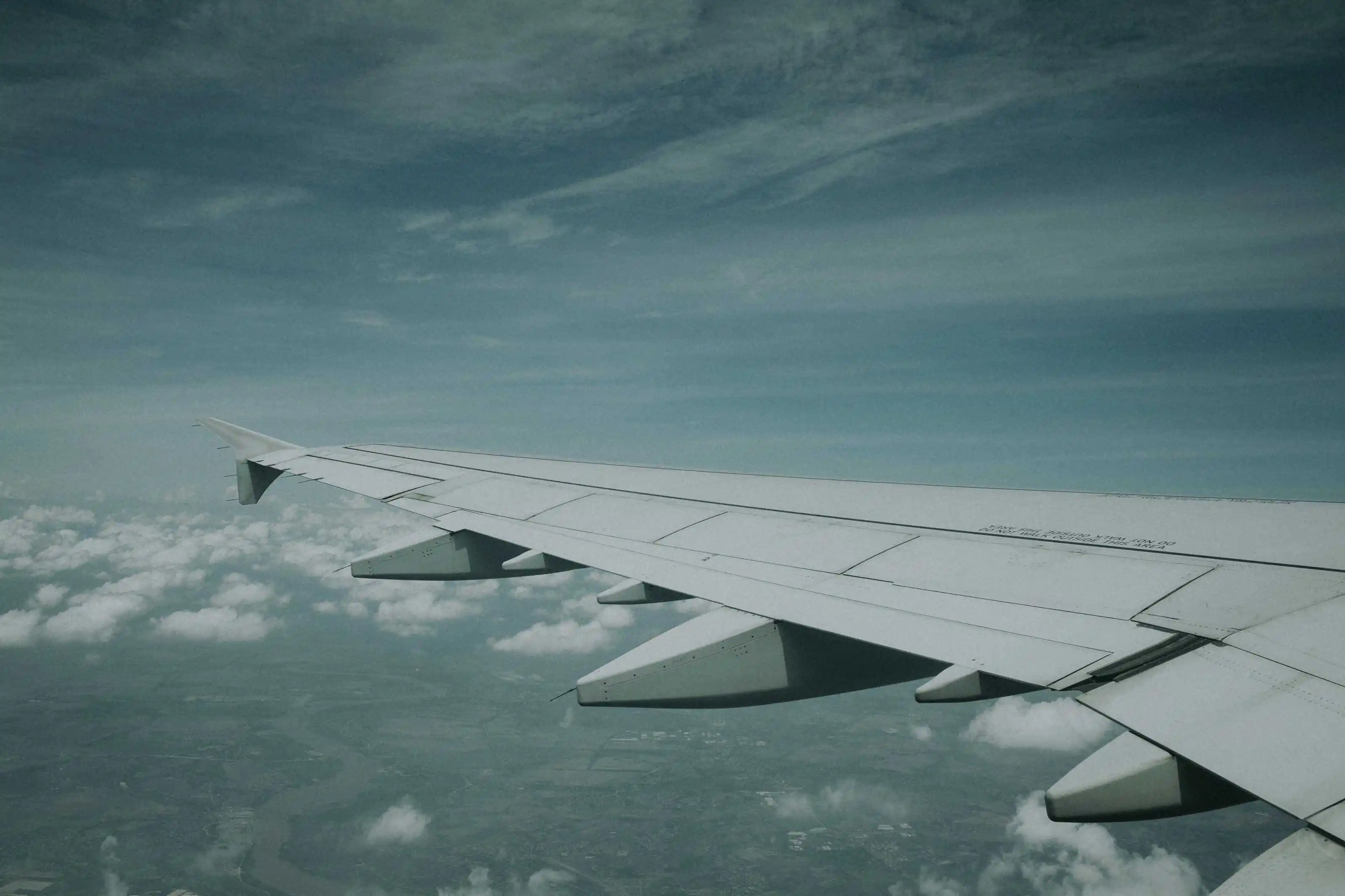 Airplane wing flying over clouds and land