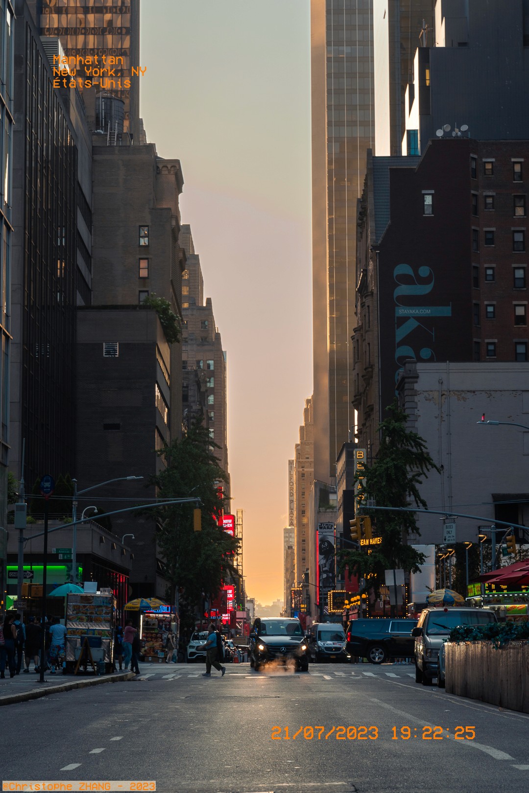 Coucher de soleil sur une rue animée de Manhattan, avec des piétons et des voitures.