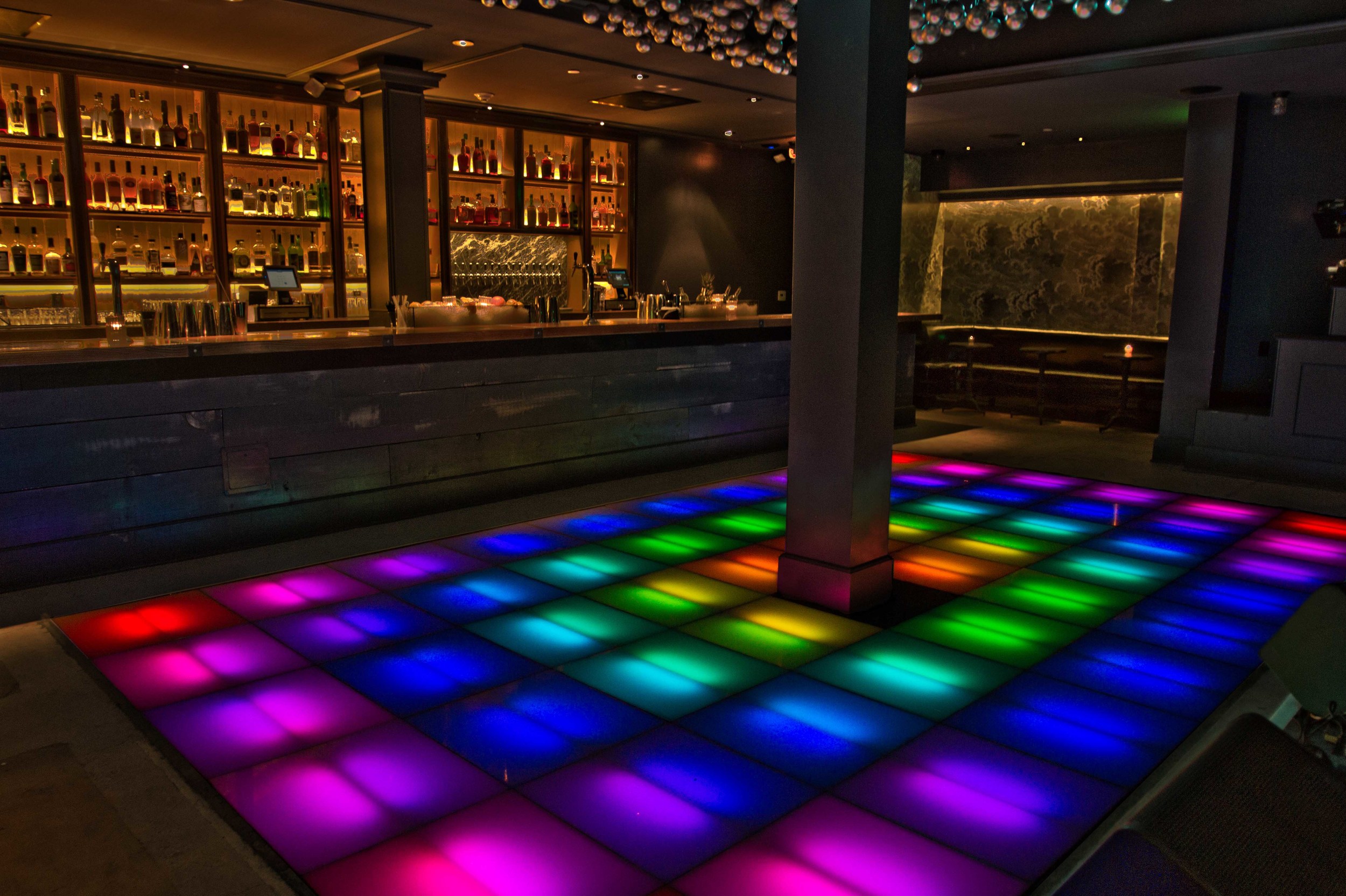 Illuminated colored dance floor beside the bar.