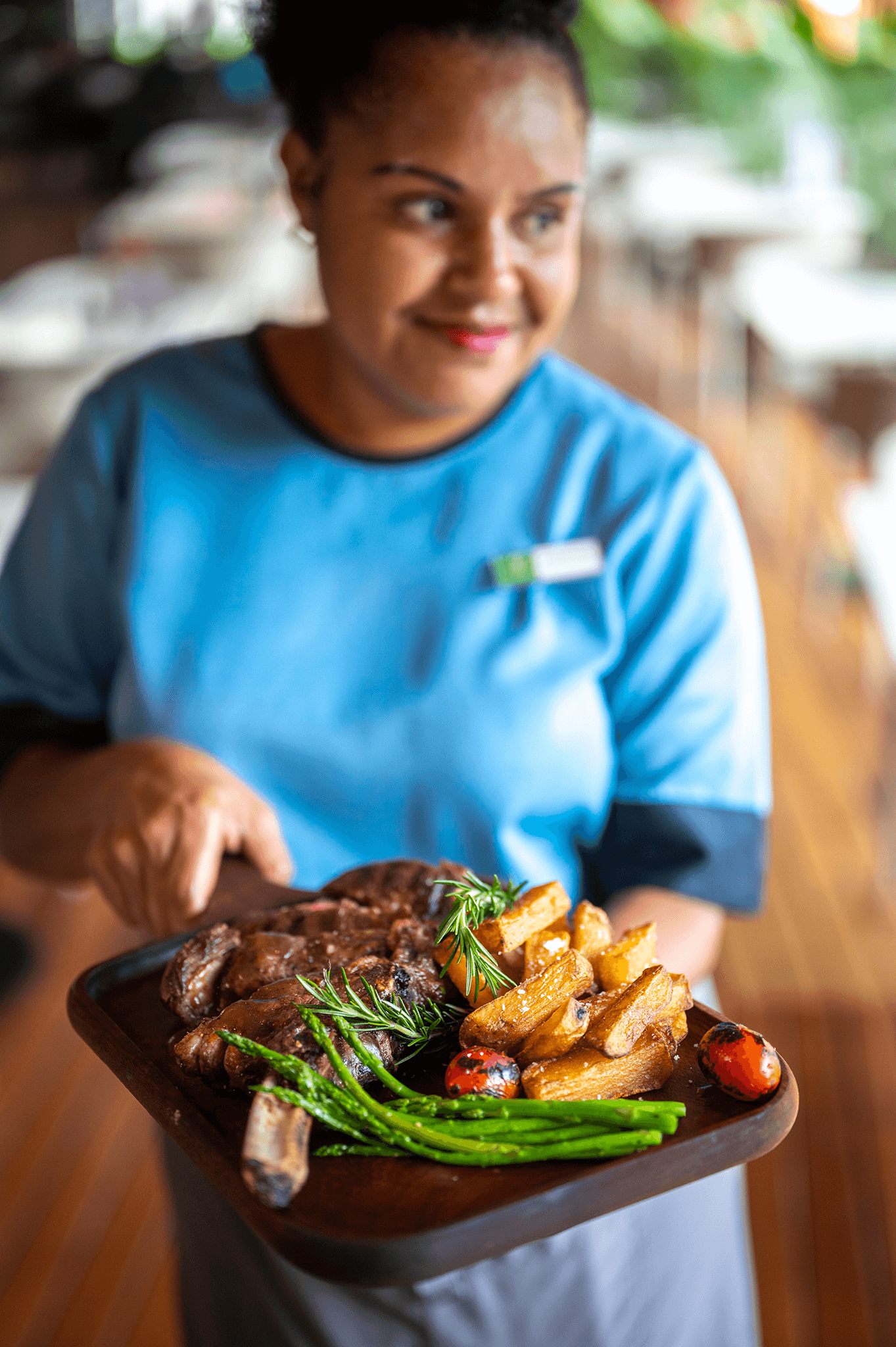 Smiling FAYA HAUS staff member presenting a hearty steak and fries meal on a tray.