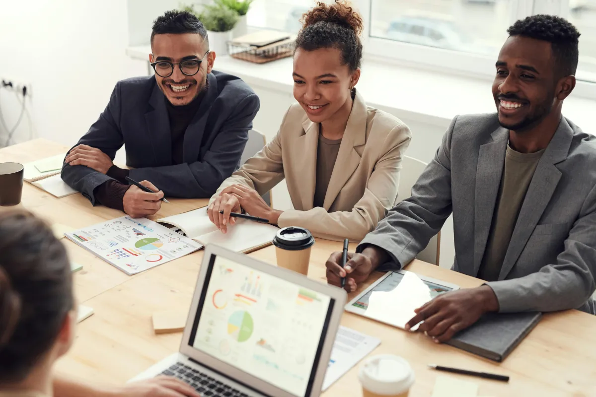 Diverse group of professionals in a meeting discussing financial charts and data on a laptop and papers, signifying debt-free strategies and wealth building.