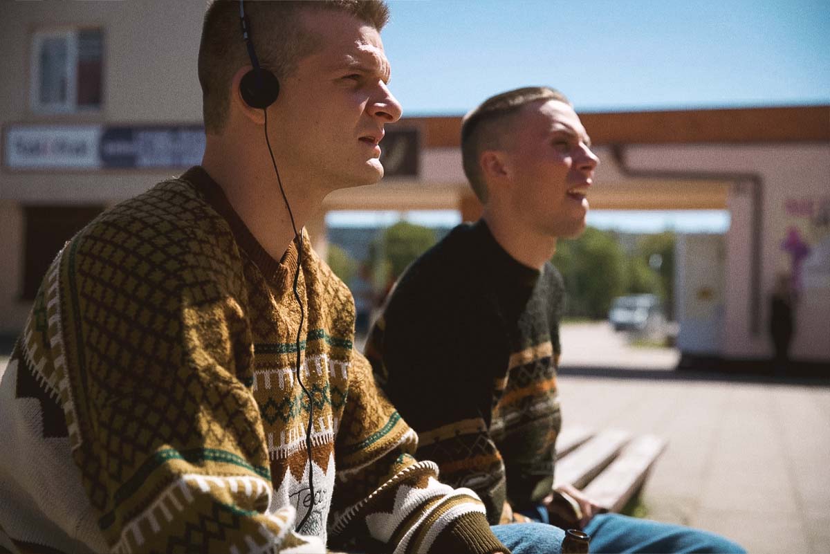 Rimants (Džiugas Grinys) and Mindė (Robertas Petraitis) listening to a retro cassette player in Southern Chronicles, a nostalgic 90s Lithuanian comedy-drama.