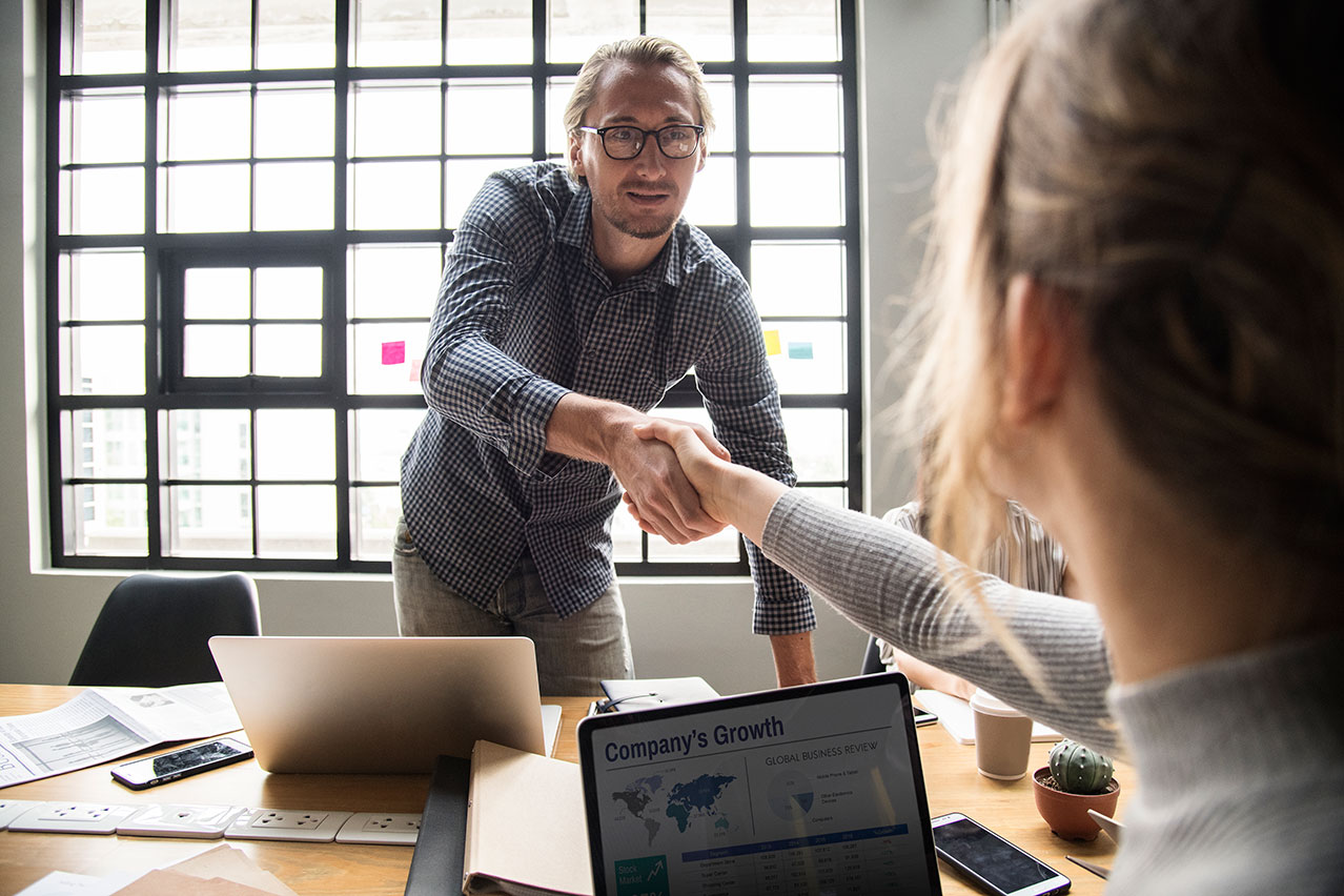 Trusting your bank is vital - man shakes hand at meeting with woman holding laptop showing business growth