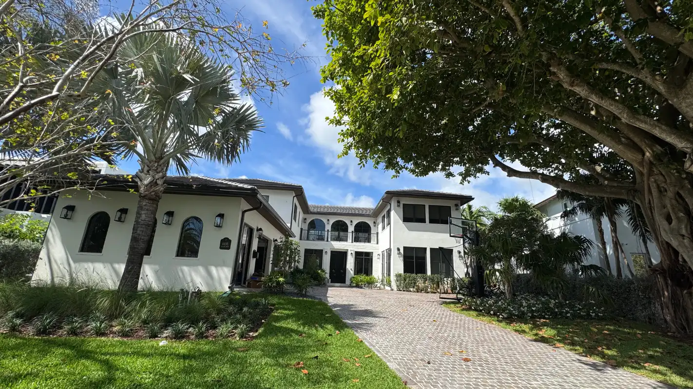 Front view of a Mediterranean-style Bay Point estate, with white stucco walls, arched windows, a paver driveway, mature shade trees, and palm-lined landscaping.